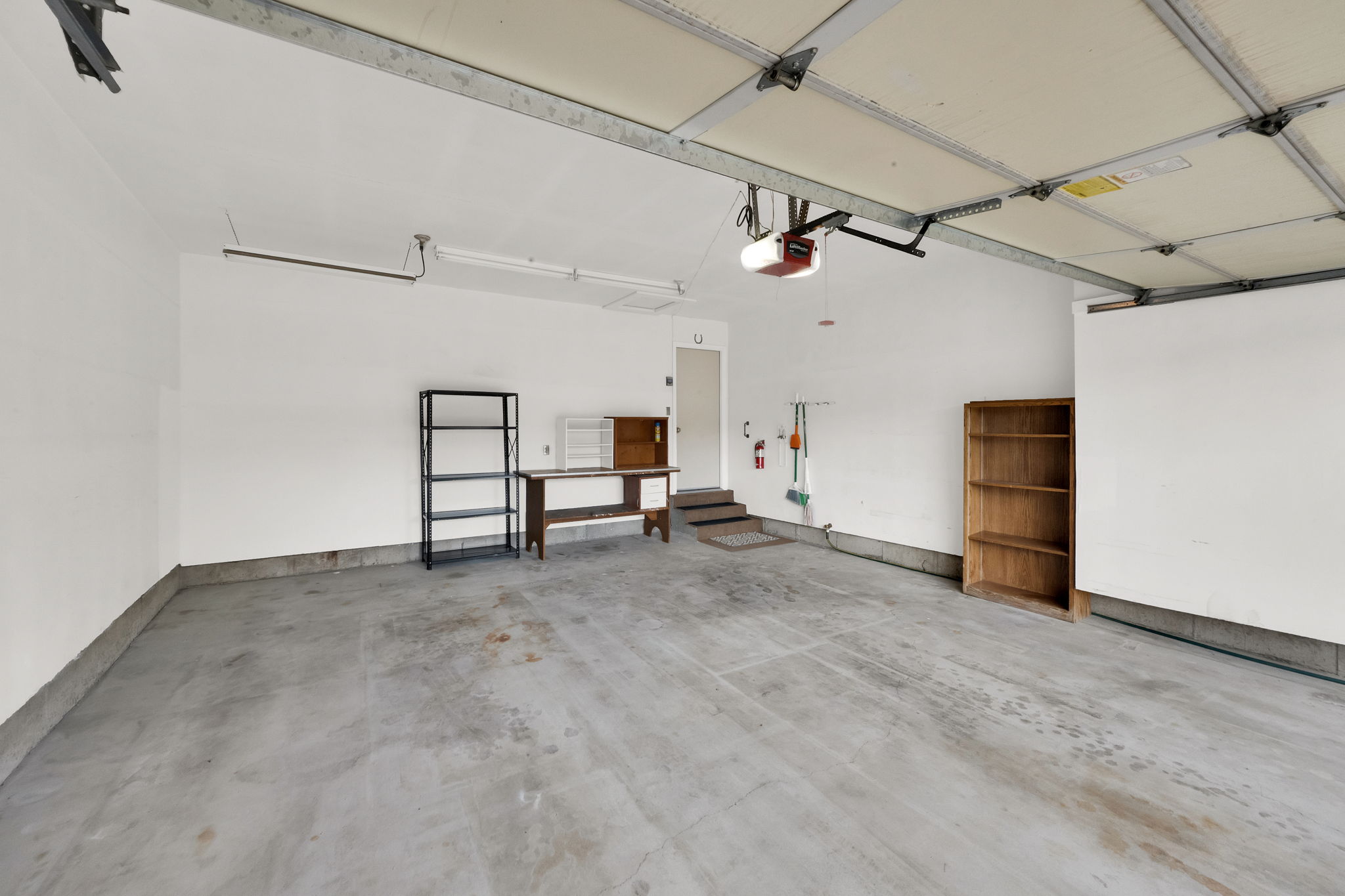 Spacious garage with concrete flooring, automatic garage door opener, and a side entry door with steps