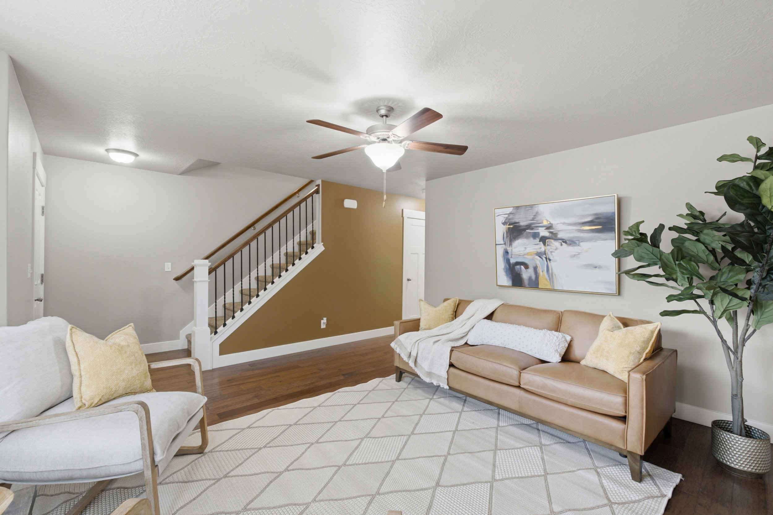 Living area featuring wood-finish flooring, a ceiling fan with integrated lighting, and a staircase with white risers and dark wood handrail