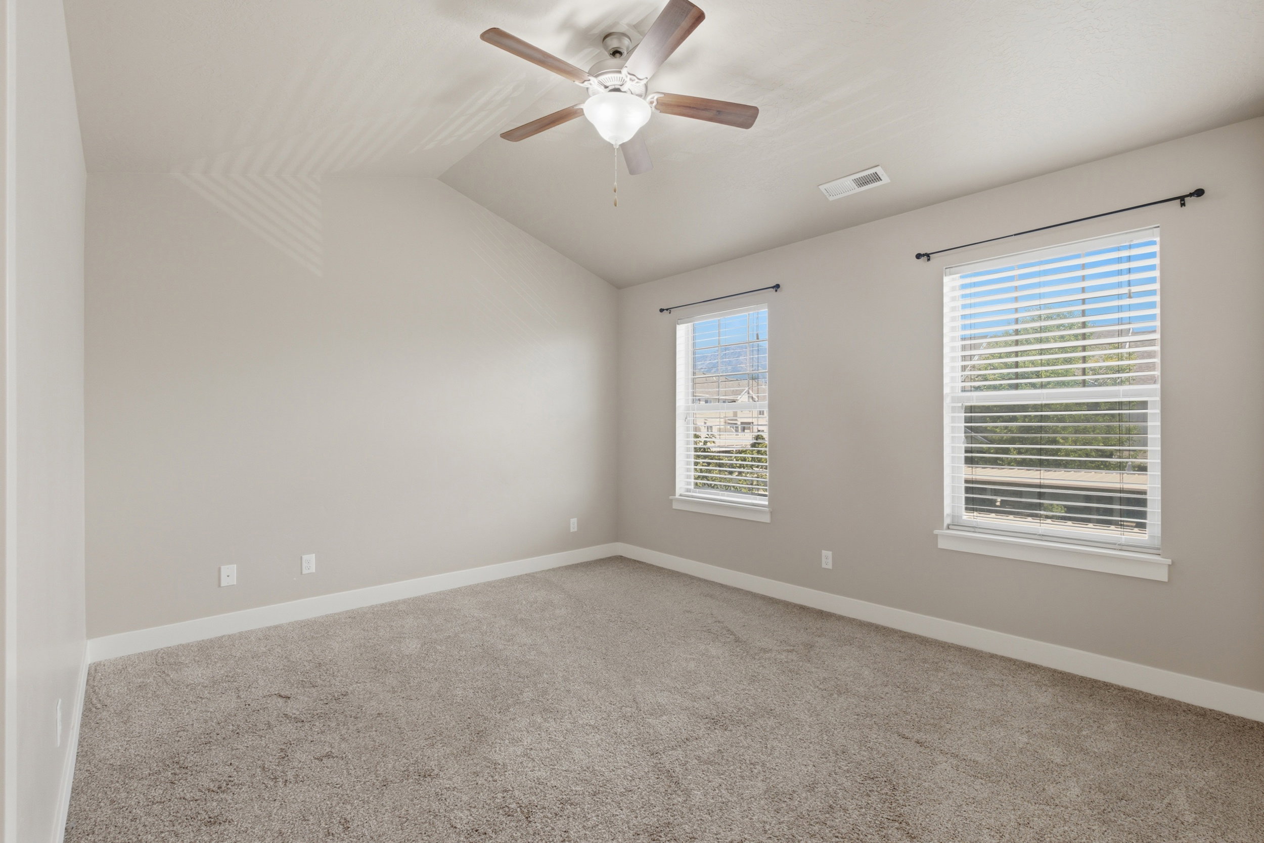 Spacious room featuring vaulted ceilings, light gray wall paint, and gray carpet flooring