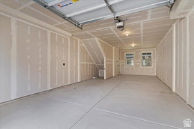 Spacious unfinished garage featuring two windows, recessed lighting, concrete flooring, and an integrated stairway