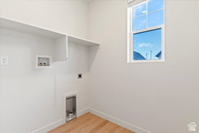 Dedicated utility space featuring a single window, built-in shelving, washer hookups, dryer vent, and wood-finish flooring