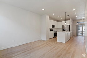 Open-concept living area featuring light wood-finish flooring, recessed lighting, and a white kitchen with stainless steel appliances