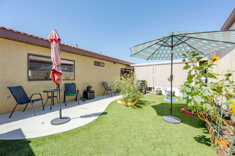 Backyard featuring a synthetic turf lawn, concrete pathway, stucco exterior, and raised garden beds