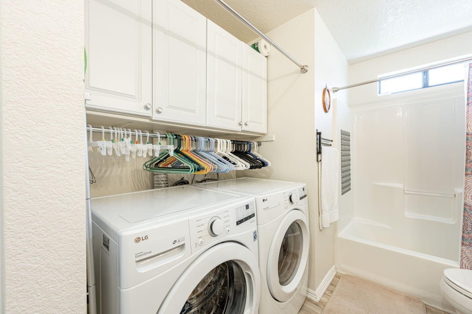 Utility space featuring built-in white cabinetry, a hanging rod, wood-finish flooring, a white bathtub with shower, and an upper window