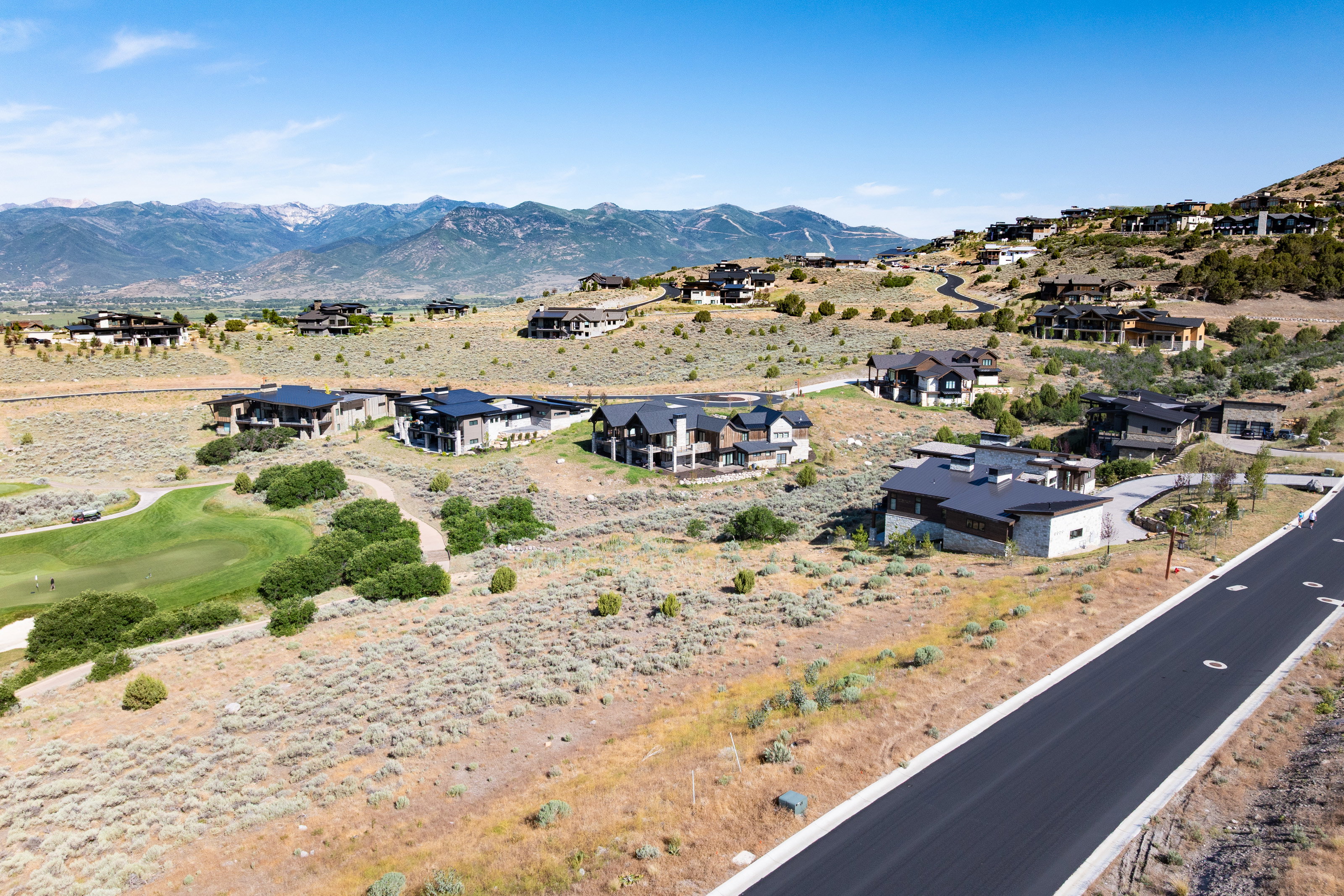 Expansive residential development featuring modern architecture, mountain backdrop, paved roadways, and proximity to a golf course