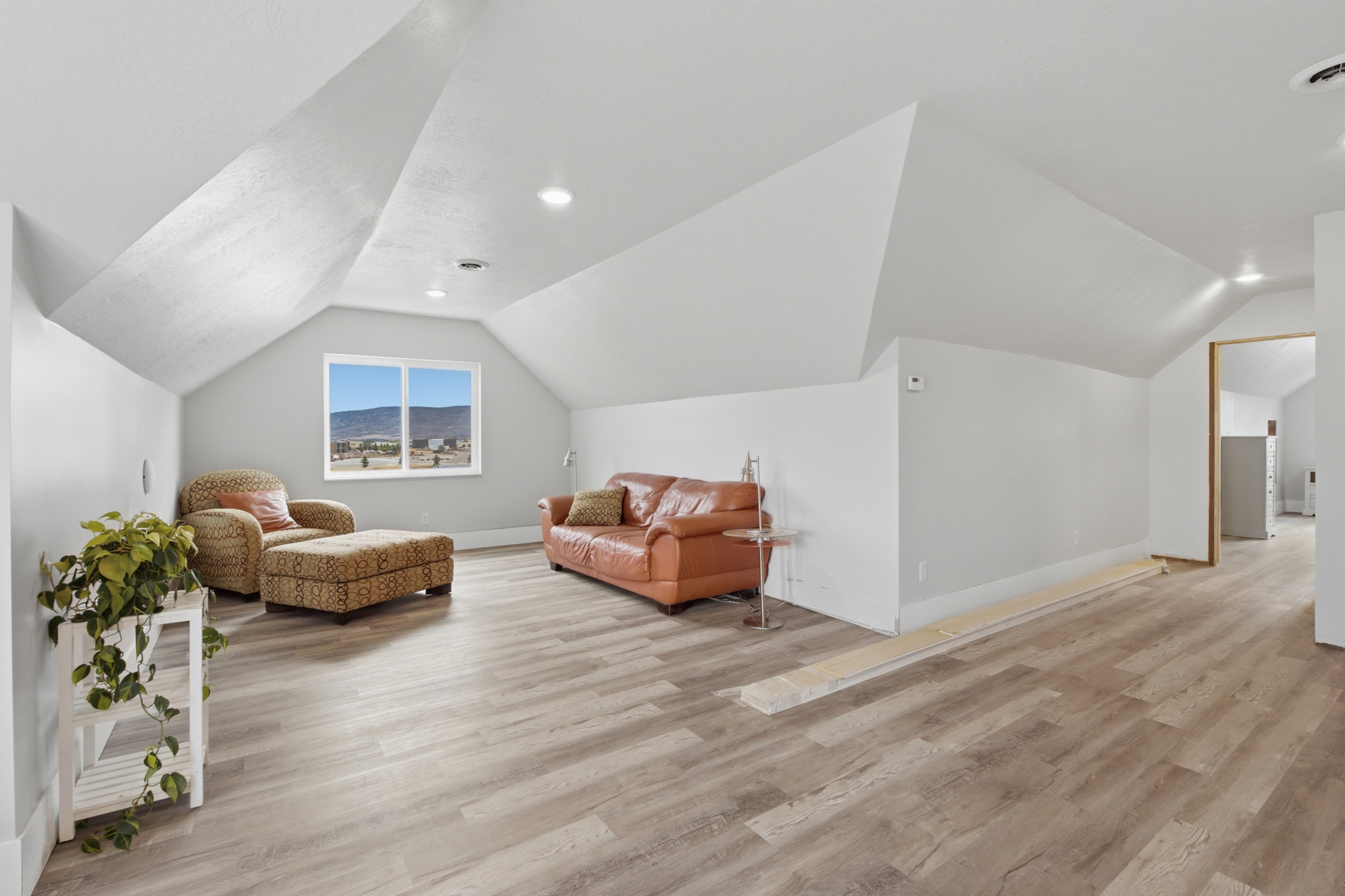 Spacious open room featuring a large window, wood-finish flooring, recessed lighting, and sloped ceilings
