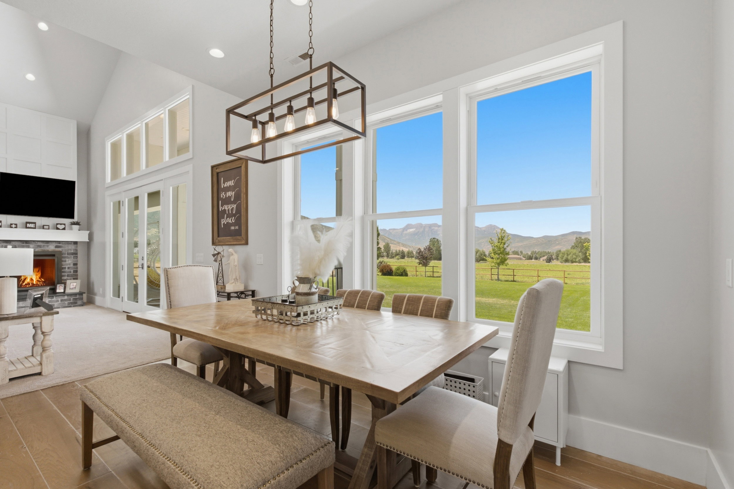 Dining area featuring a rectangular wood-finish table, a linear chandelier, and expansive windows showcasing a mountain backdrop