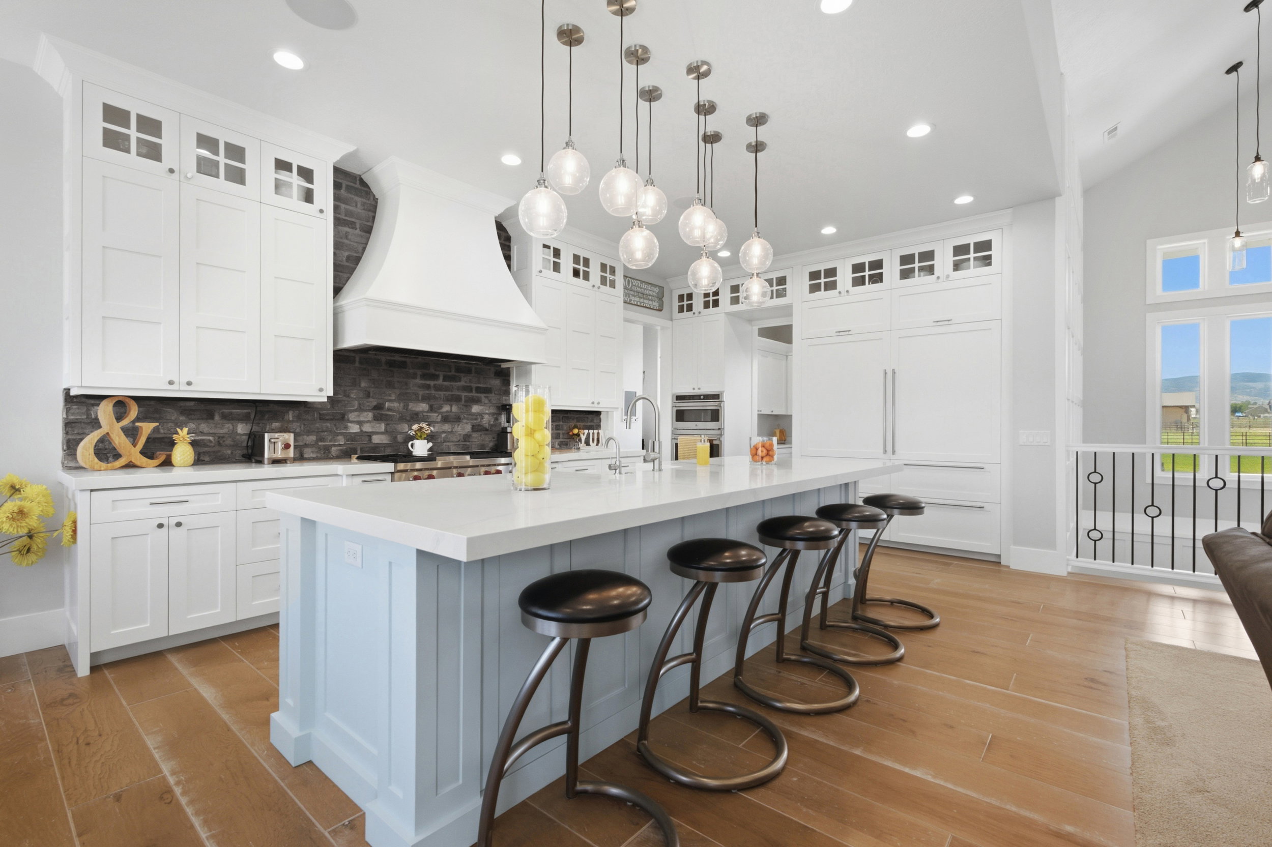 Gourmet kitchen featuring a light blue island with seating, white shaker cabinetry, a custom range hood, dark brick-style backsplash, and wood-finish flooring