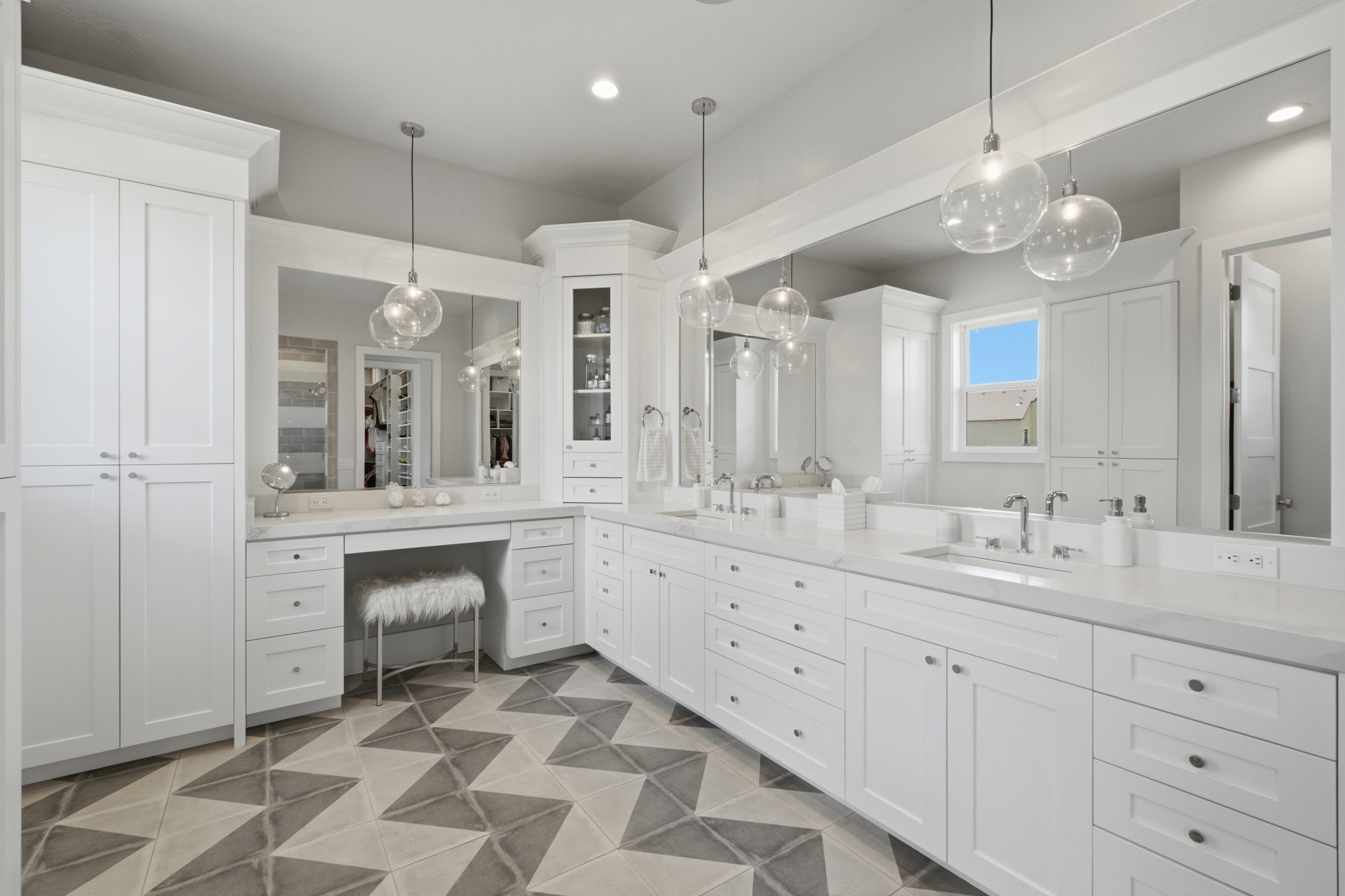 Expansive vanity area featuring dual sinks set in a white countertop, extensive white cabinetry, and a dedicated vanity with a large mirror
