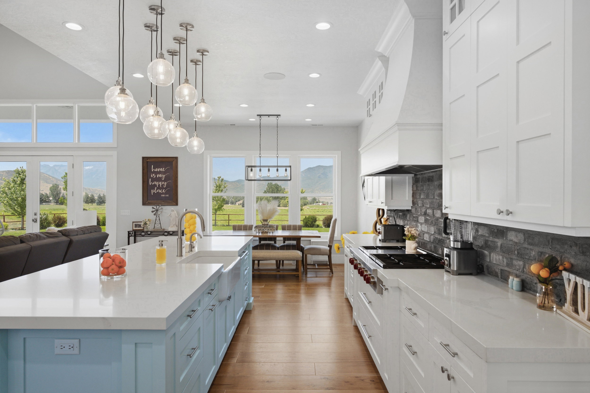 Spacious kitchen featuring a light blue island with an undermount sink, white countertops, a brick-patterned backsplash, white shaker-style cabinetry, and wood-finish flooring