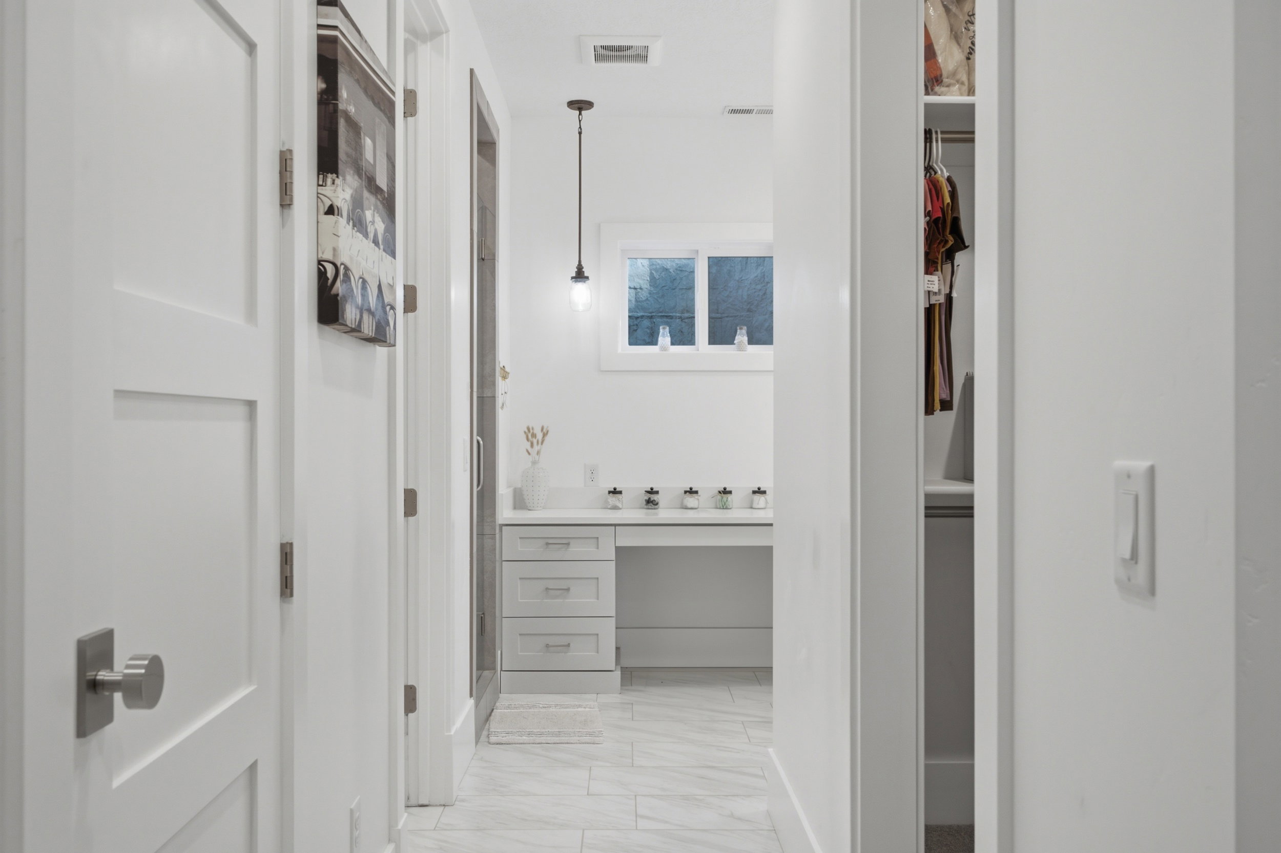 White bathroom vanity with built-in desk, under-mount sink, and contemporary pendant lighting