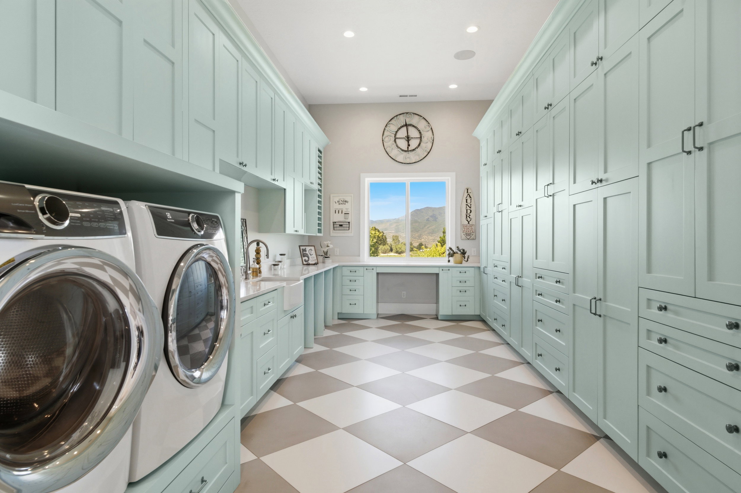 Spacious utility room featuring extensive light teal cabinetry, a built-in workstation, a large window, a farmhouse sink, and checkered tile flooring