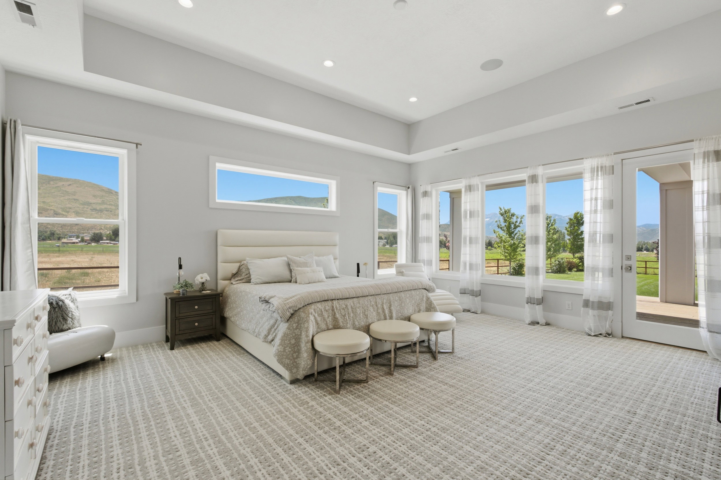 Spacious room featuring a tray ceiling with recessed lighting, multiple large windows, and a glass-paneled door opening to an outdoor area