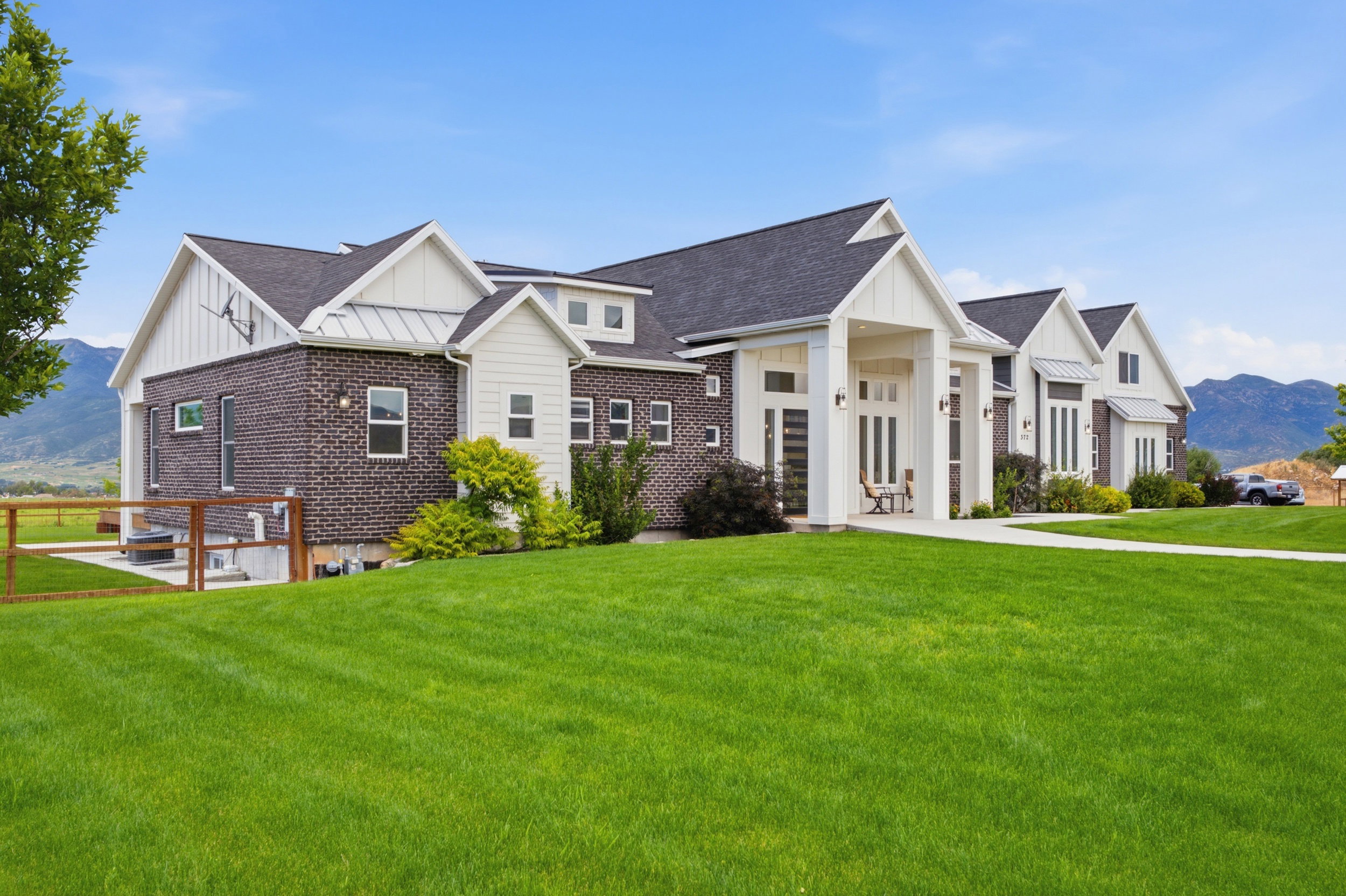 Modern ranch-style home featuring a dark brick facade, white vertical siding accents, a prominent covered entry with columns, multiple gables, and a wide front lawn