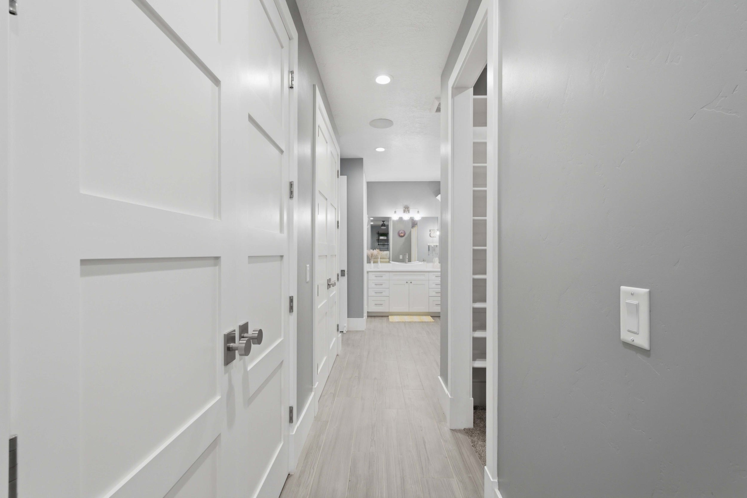 Hallway featuring light wood-finish flooring, white paneled doors with brushed nickel hardware, light grey painted walls, and recessed lighting