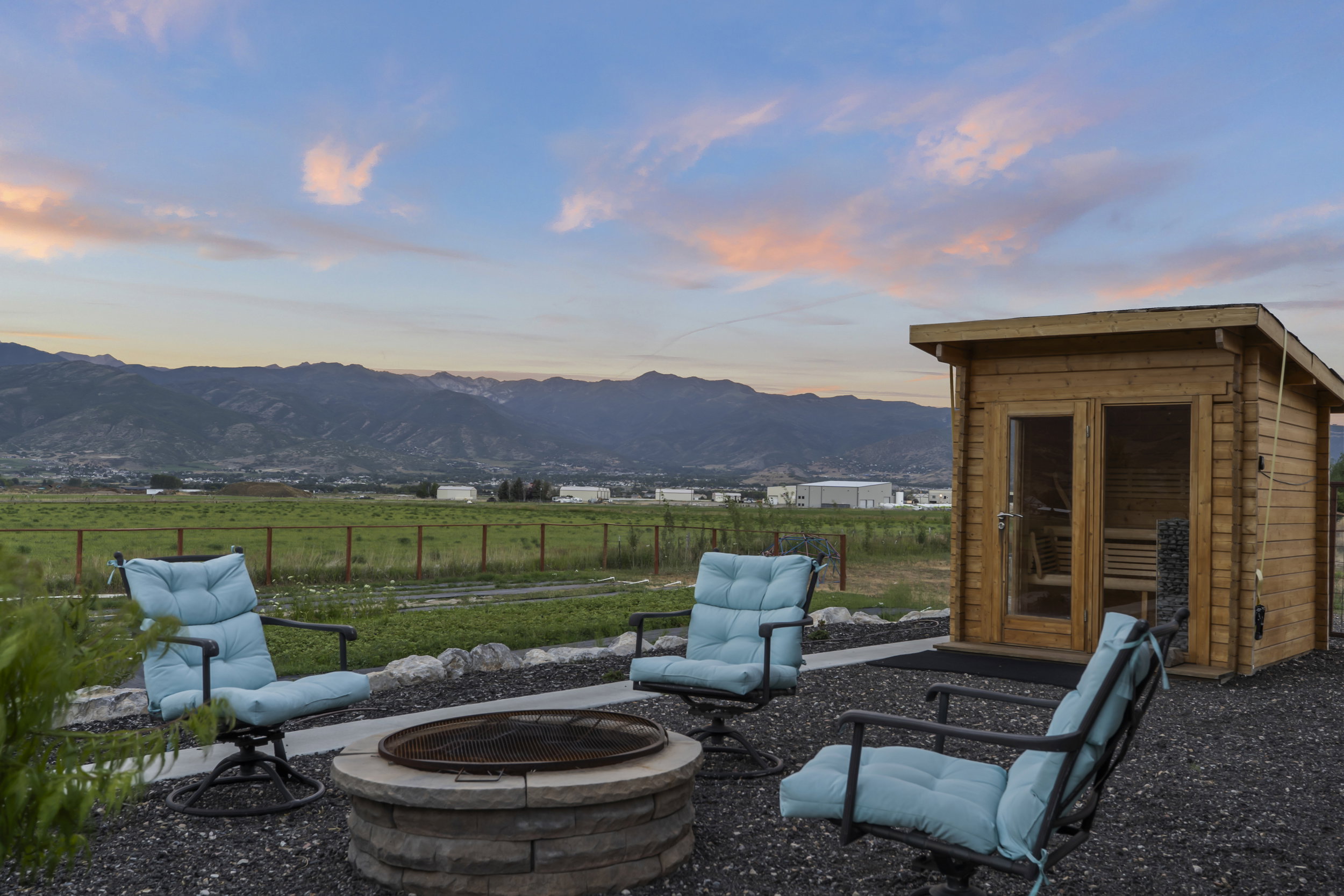 Outdoor living area featuring a stone-clad fire pit, a gravel patio, and a standalone wooden sauna structure with glass-paned doors