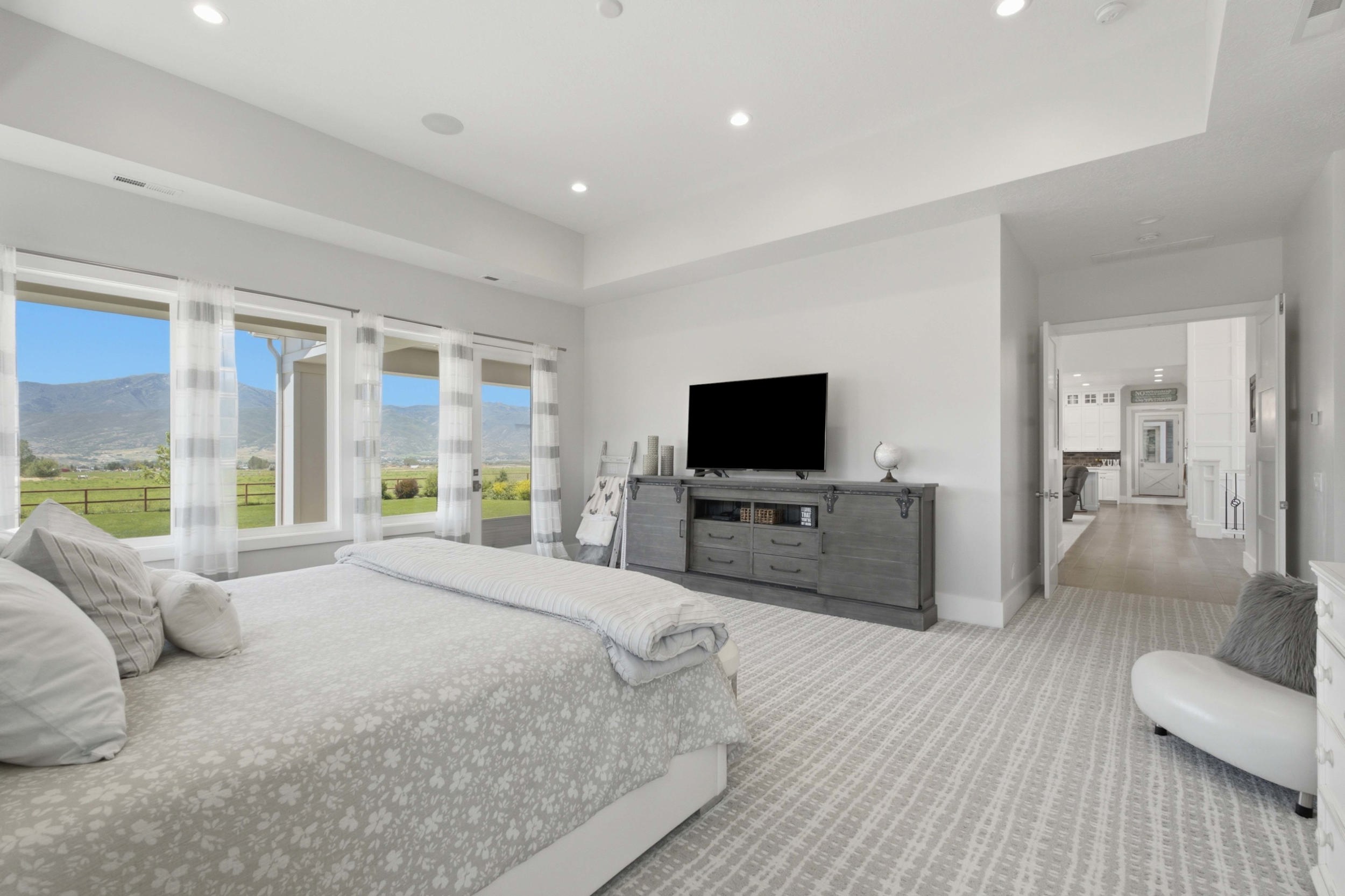 Spacious bedroom featuring a series of large windows, recessed ceiling lighting, tray ceiling, and light-toned patterned carpeting