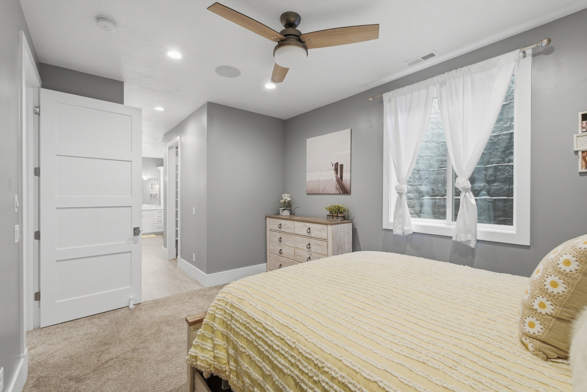Neutral-toned bedroom with a wood-finish ceiling fan, recessed lighting, and a window with white trim