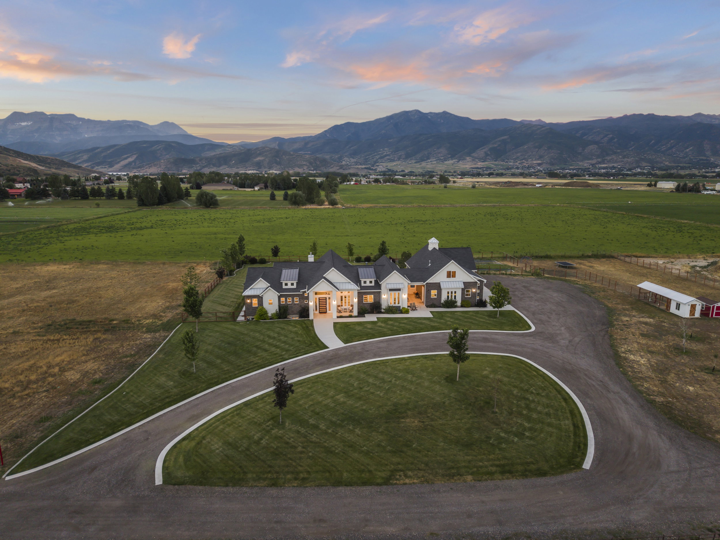 Modern farmhouse architecture featuring a white exterior with dark trim and stone accents, a multi-gabled roofline, and a prominent front entry porch