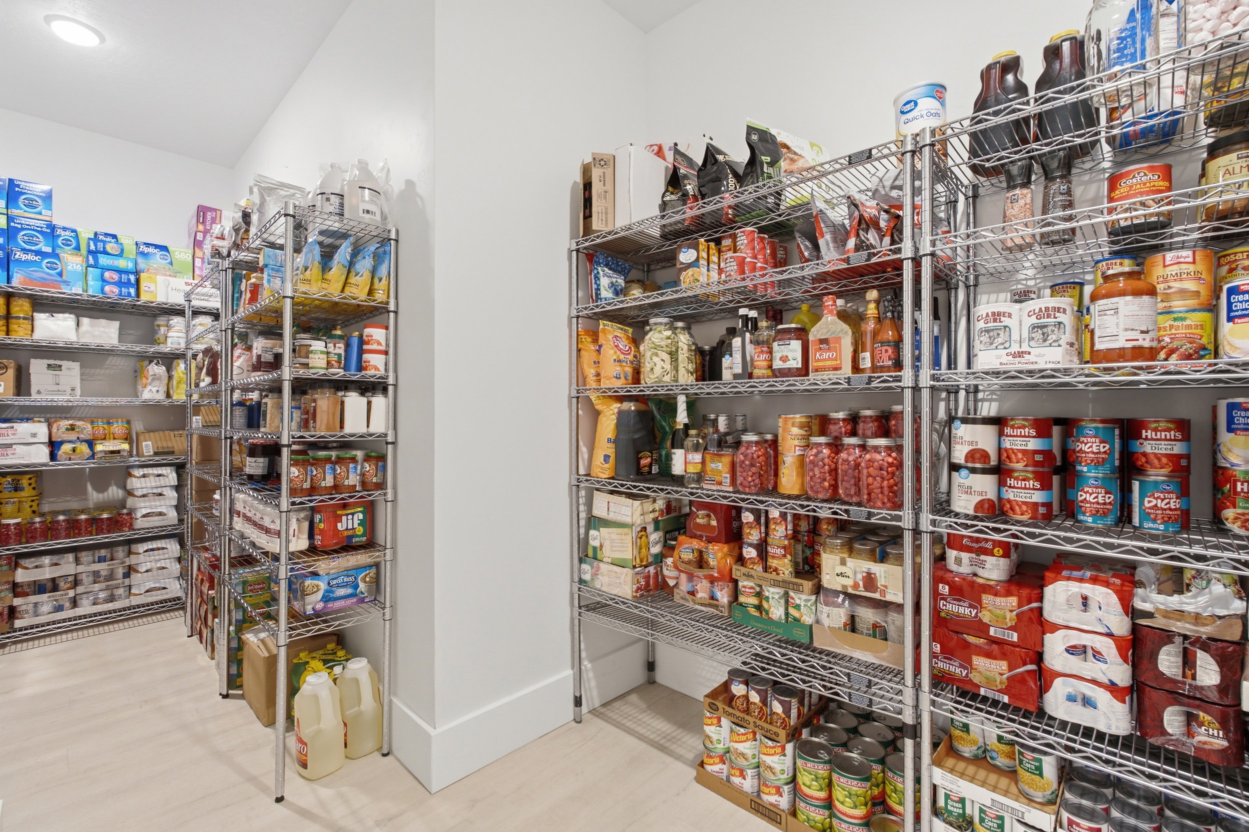 Spacious pantry featuring multiple chrome wire shelving units, light wood-finish flooring, and recessed ceiling lighting