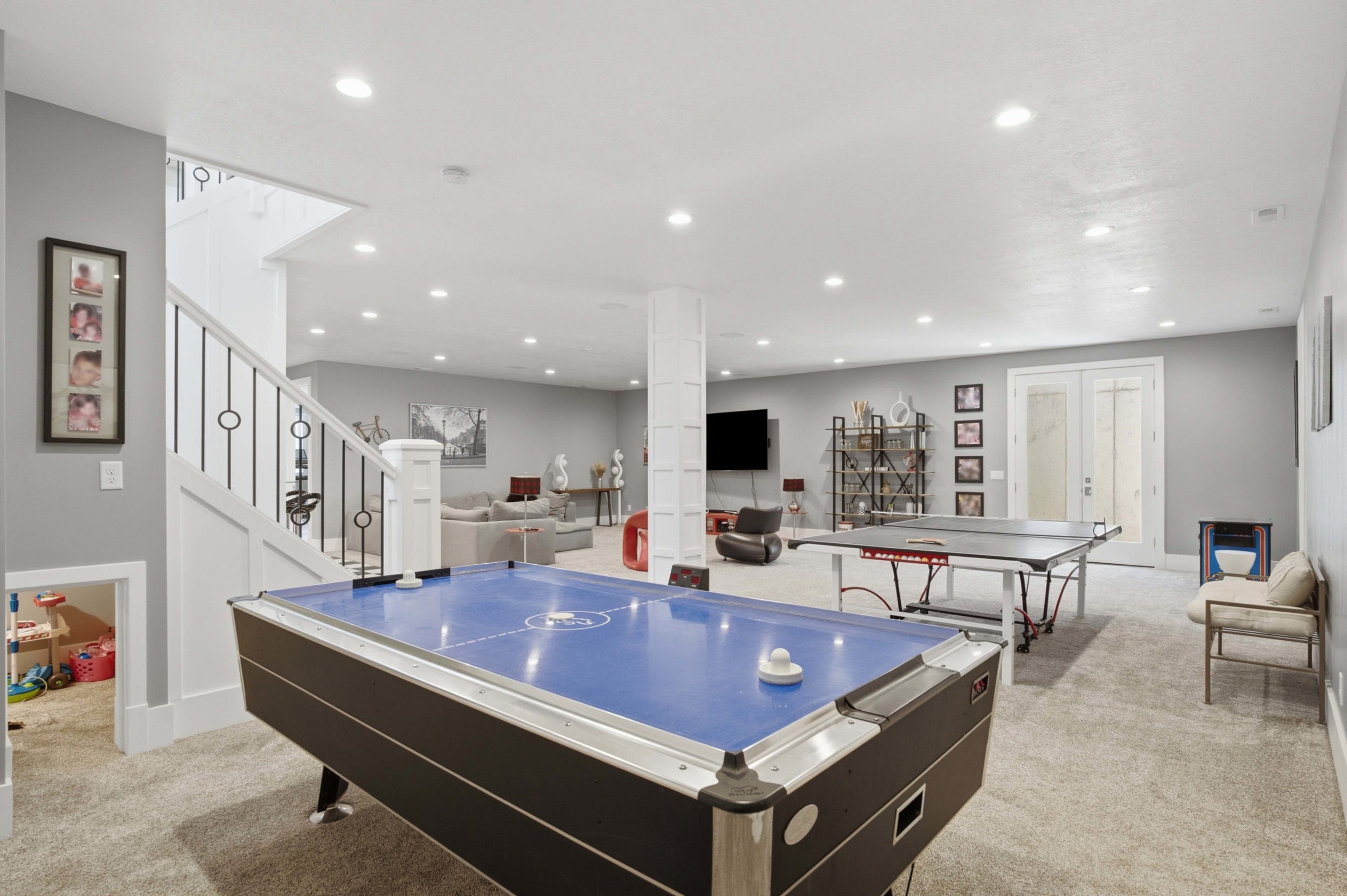 Spacious lower level featuring an open layout, plush carpeting, recessed lighting, double French doors, and a staircase with decorative iron balusters