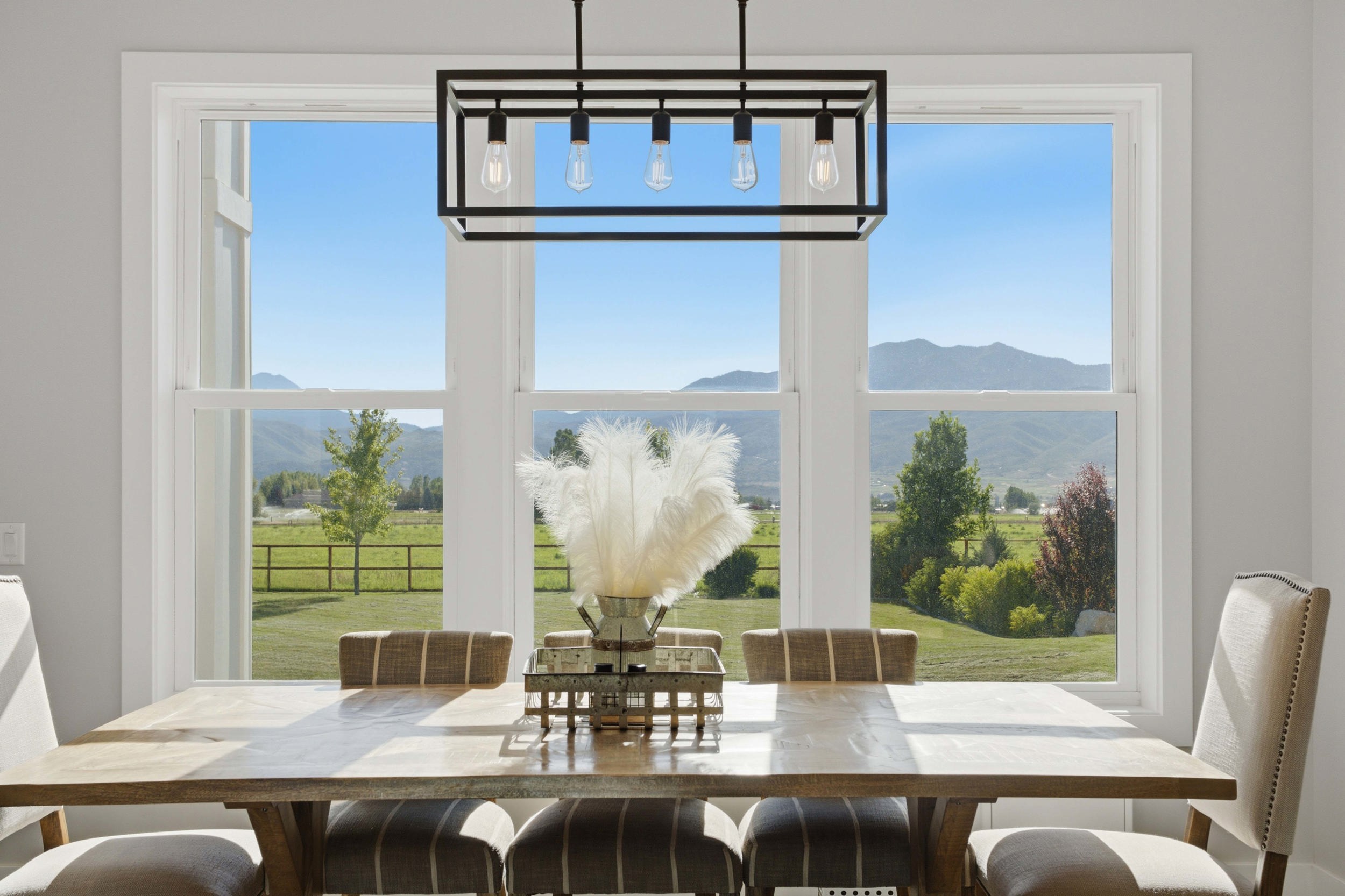 Expansive multi-pane window offering panoramic mountain scenery and green pasture