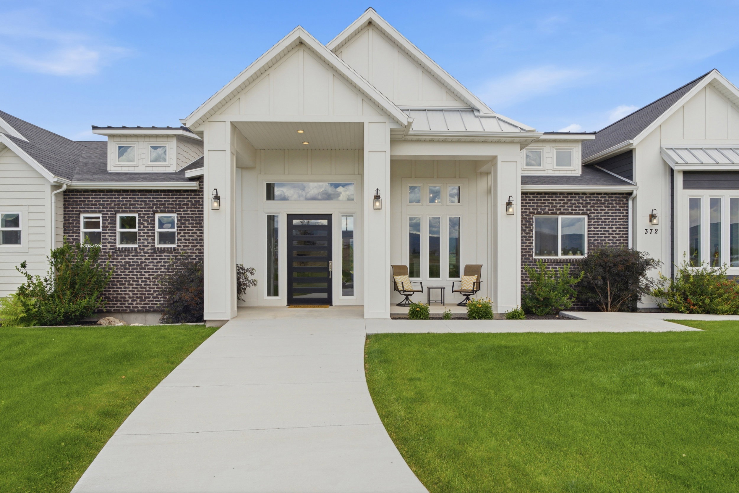 Modern farmhouse exterior featuring vertical white siding, dark brick accents, a prominent covered entry with columns, and a contemporary glass-paneled front door