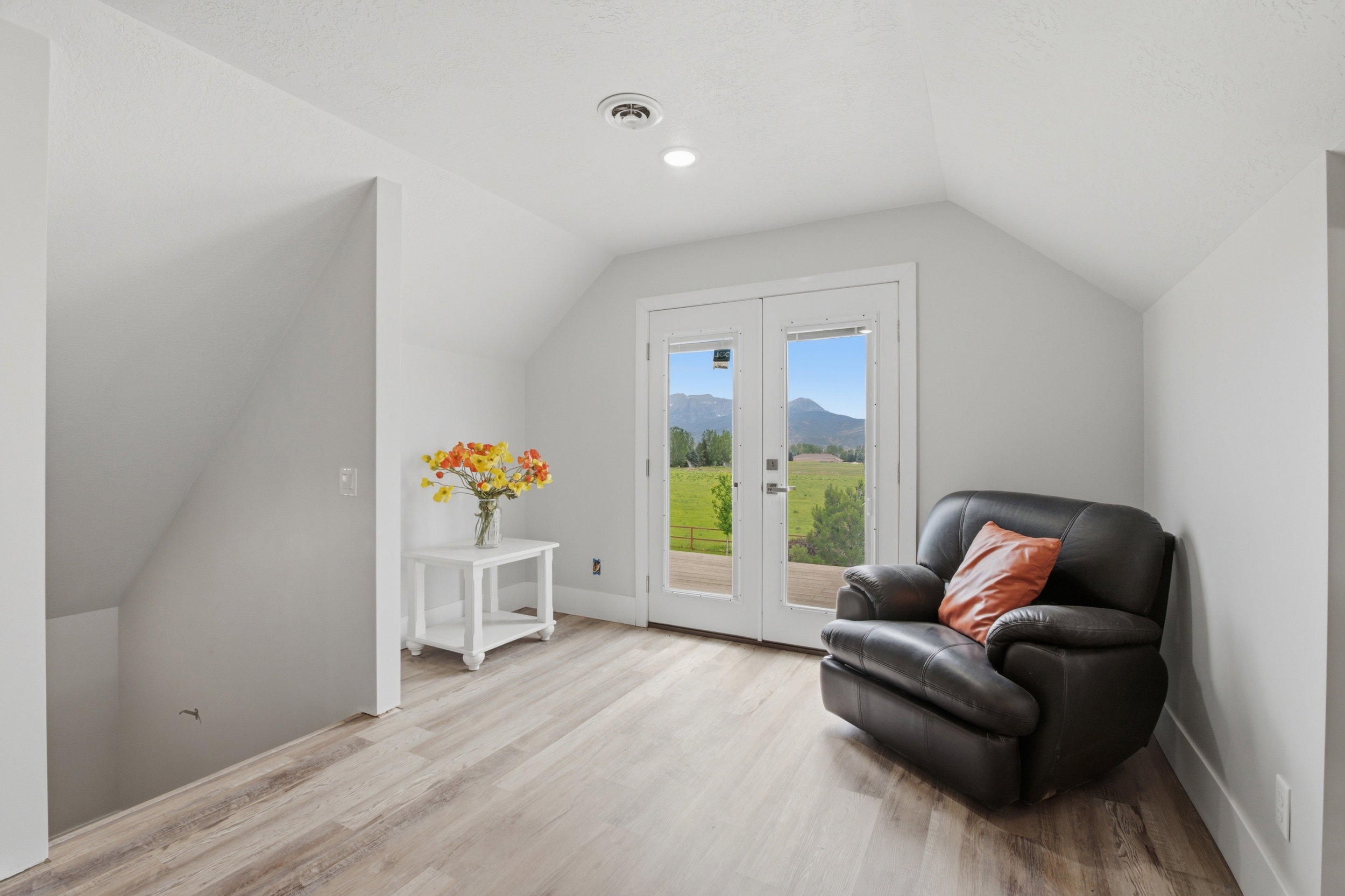 Upper-level space featuring vaulted ceilings, wood-finish flooring, recessed lighting, and white French doors opening to an exterior landscape