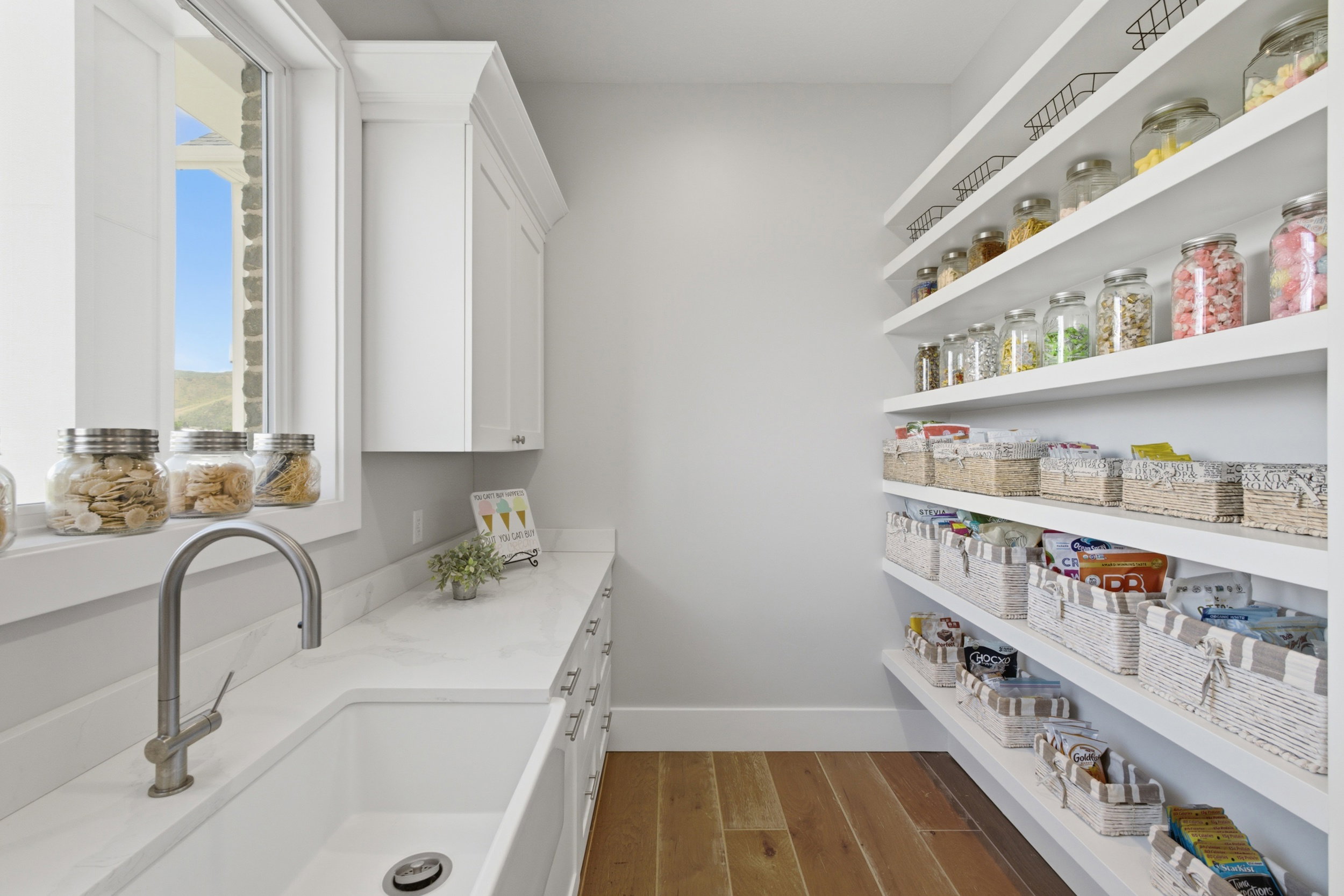 Bright pantry featuring extensive open shelving, wood-finish flooring, white cabinetry, a large sink, and a window