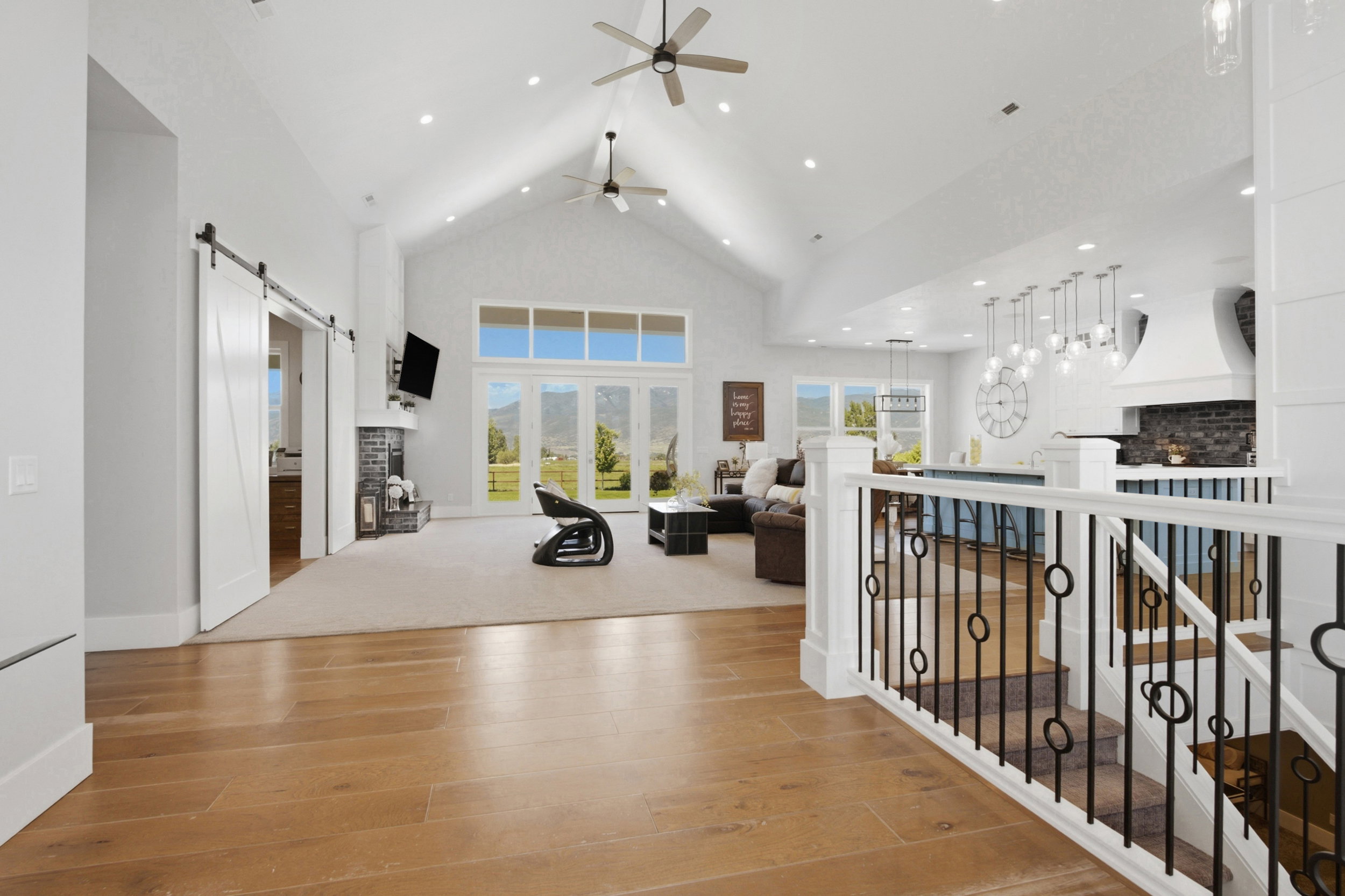 Open-concept interior featuring wood-finish flooring, vaulted ceilings, a prominent fireplace, a kitchen island, and a decorative staircase railing
