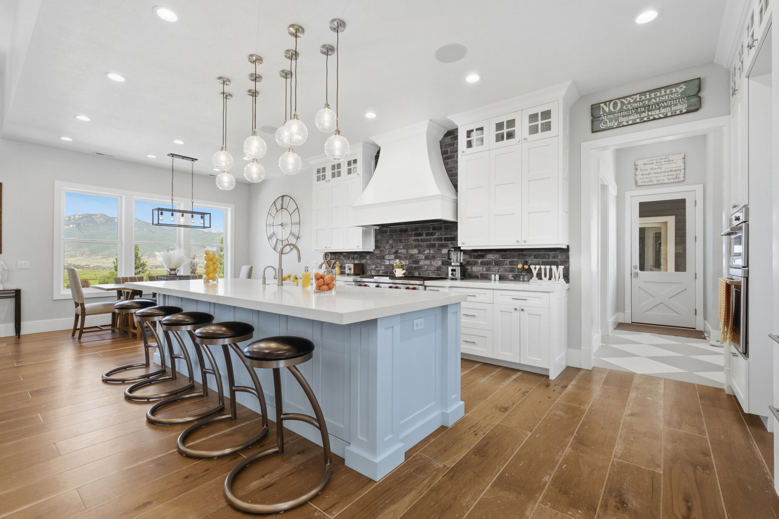 Spacious kitchen featuring a large island with seating, pendant lighting, wood-finish flooring, white cabinetry, and a dark brick-patterned backsplash