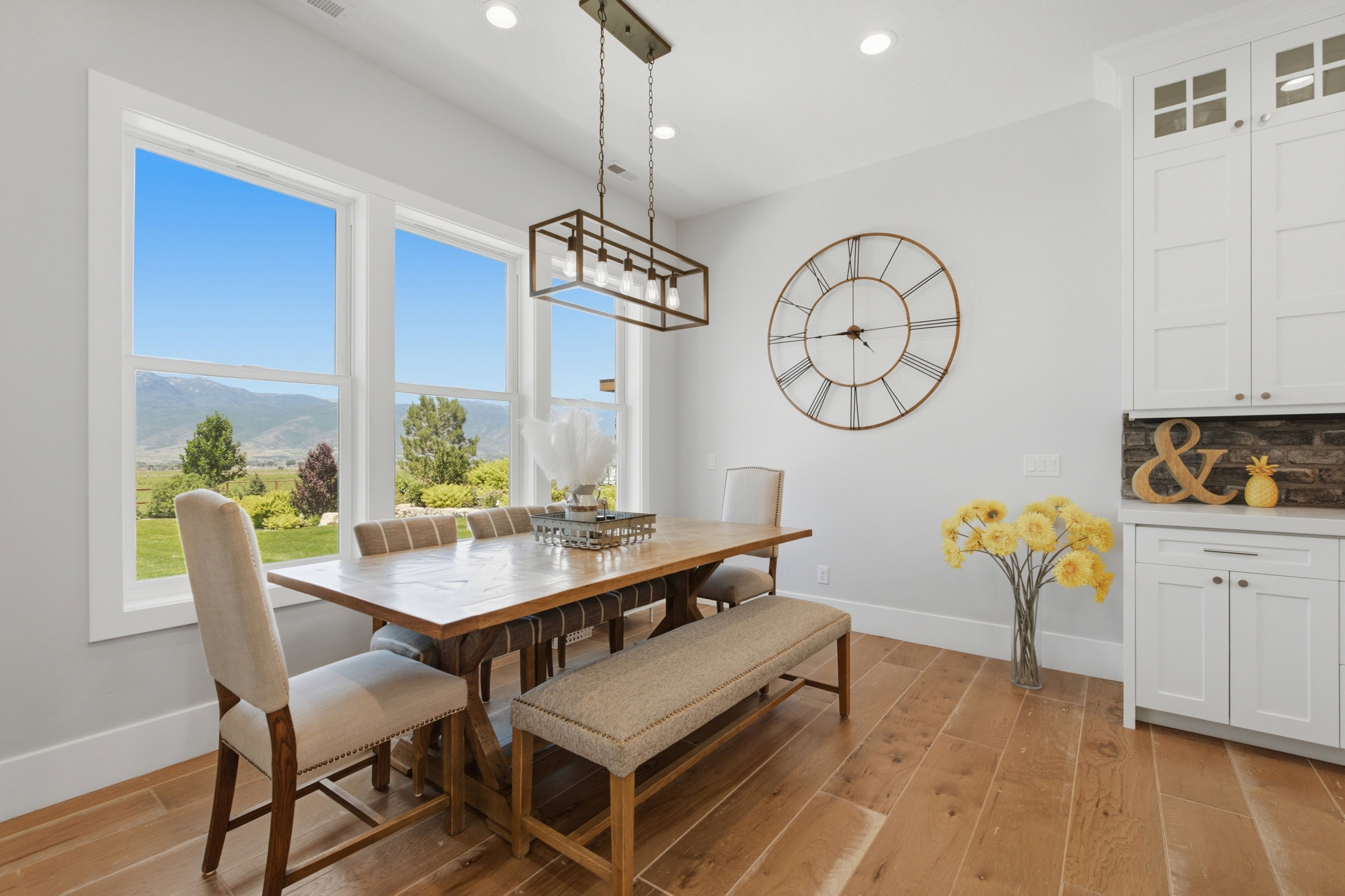 Dining area featuring large windows showcasing mountain scenery, wood-finish flooring, a contemporary chandelier, white built-in cabinetry, and a stone-effect backsplash