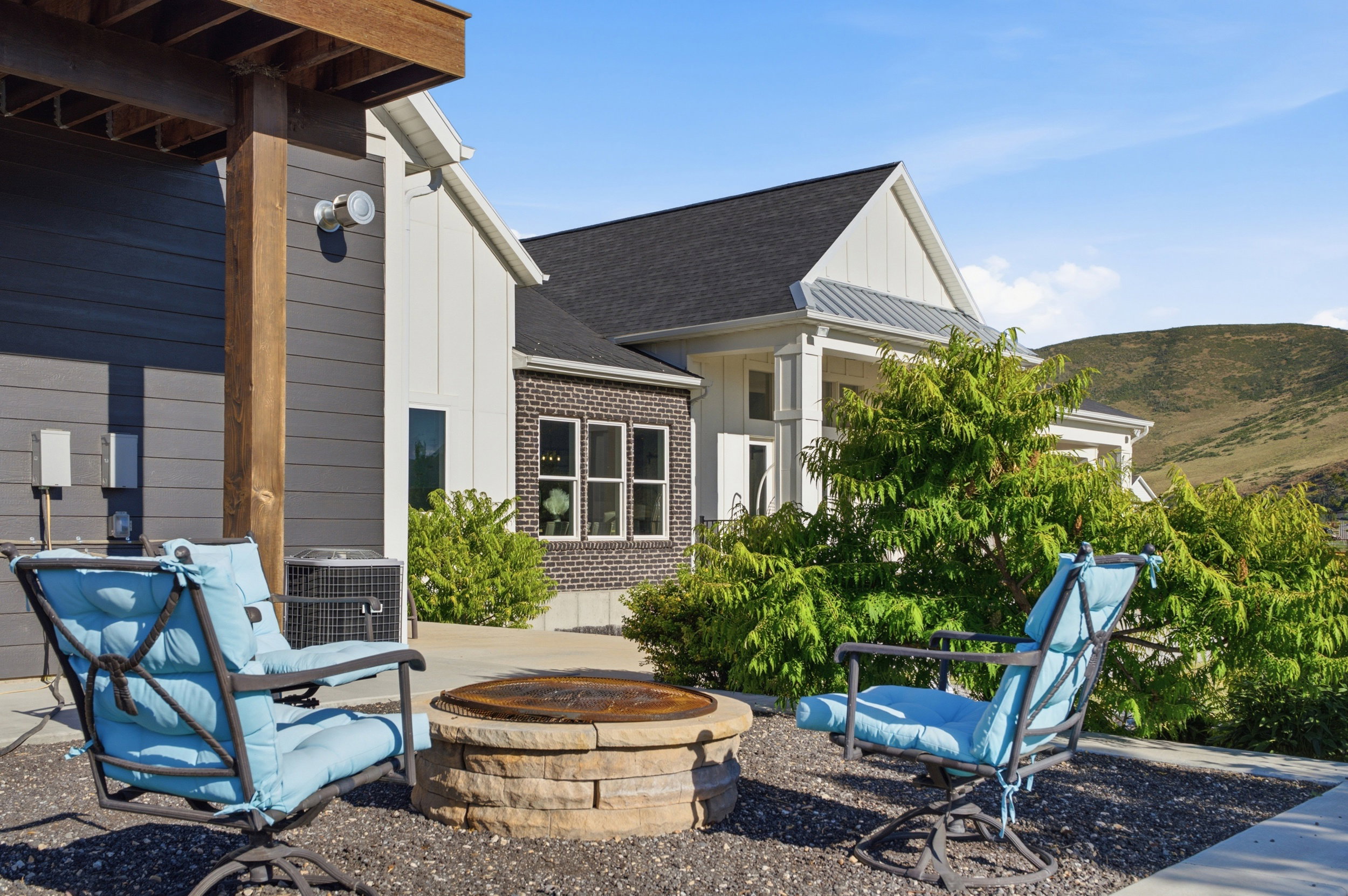 Outdoor patio featuring a built-in stone fire pit, gravel ground cover, and a partial view of the residence