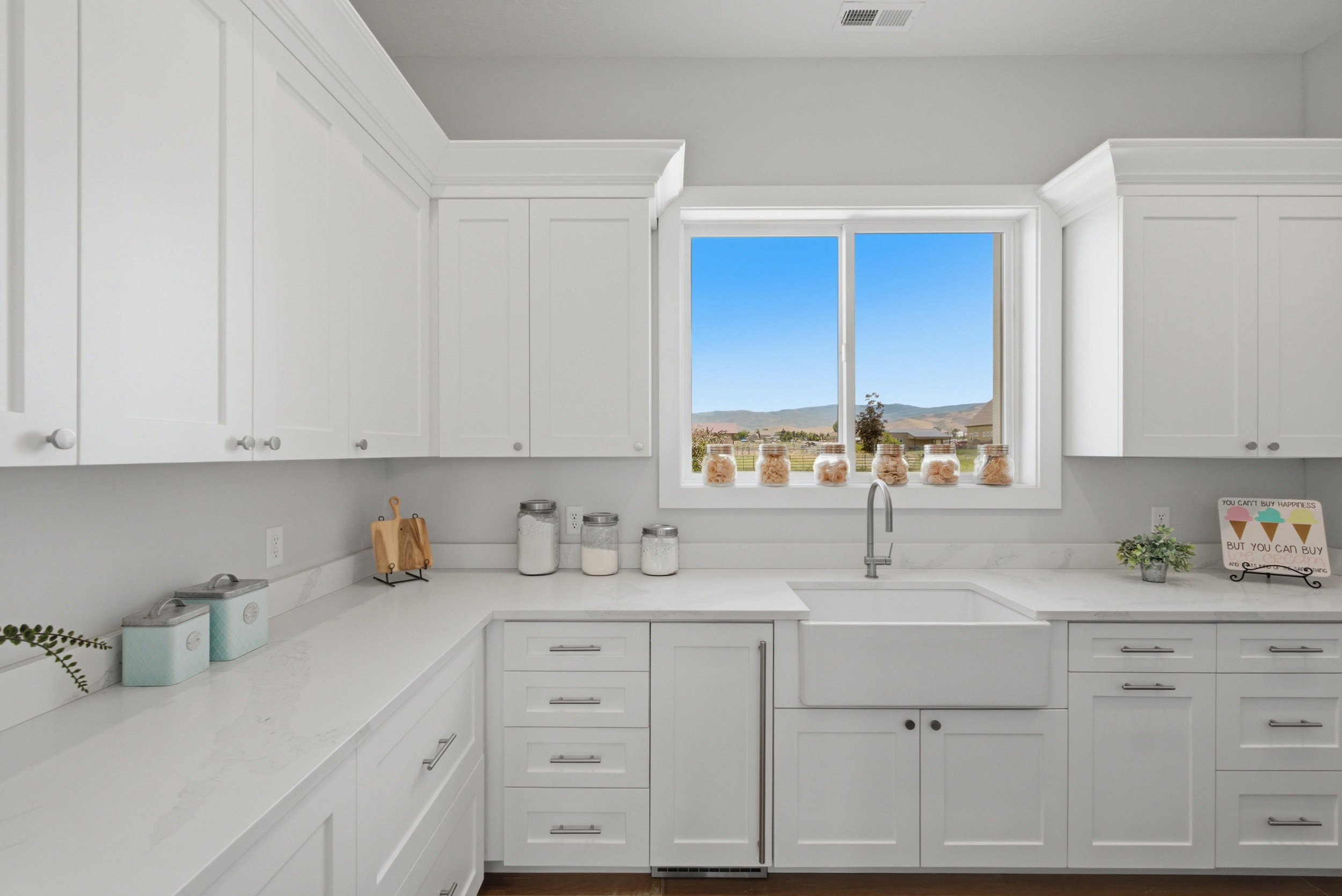 Kitchen featuring white shaker-style cabinetry, a farmhouse sink with a gooseneck faucet, light-toned countertops, and a window with a mountain backdrop