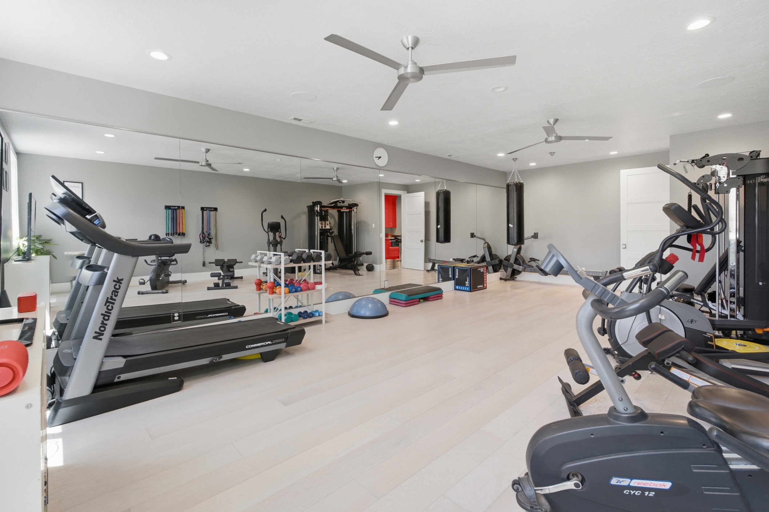 Spacious fitness room featuring light wood-finish flooring, full-wall mirrors, and two ceiling fans