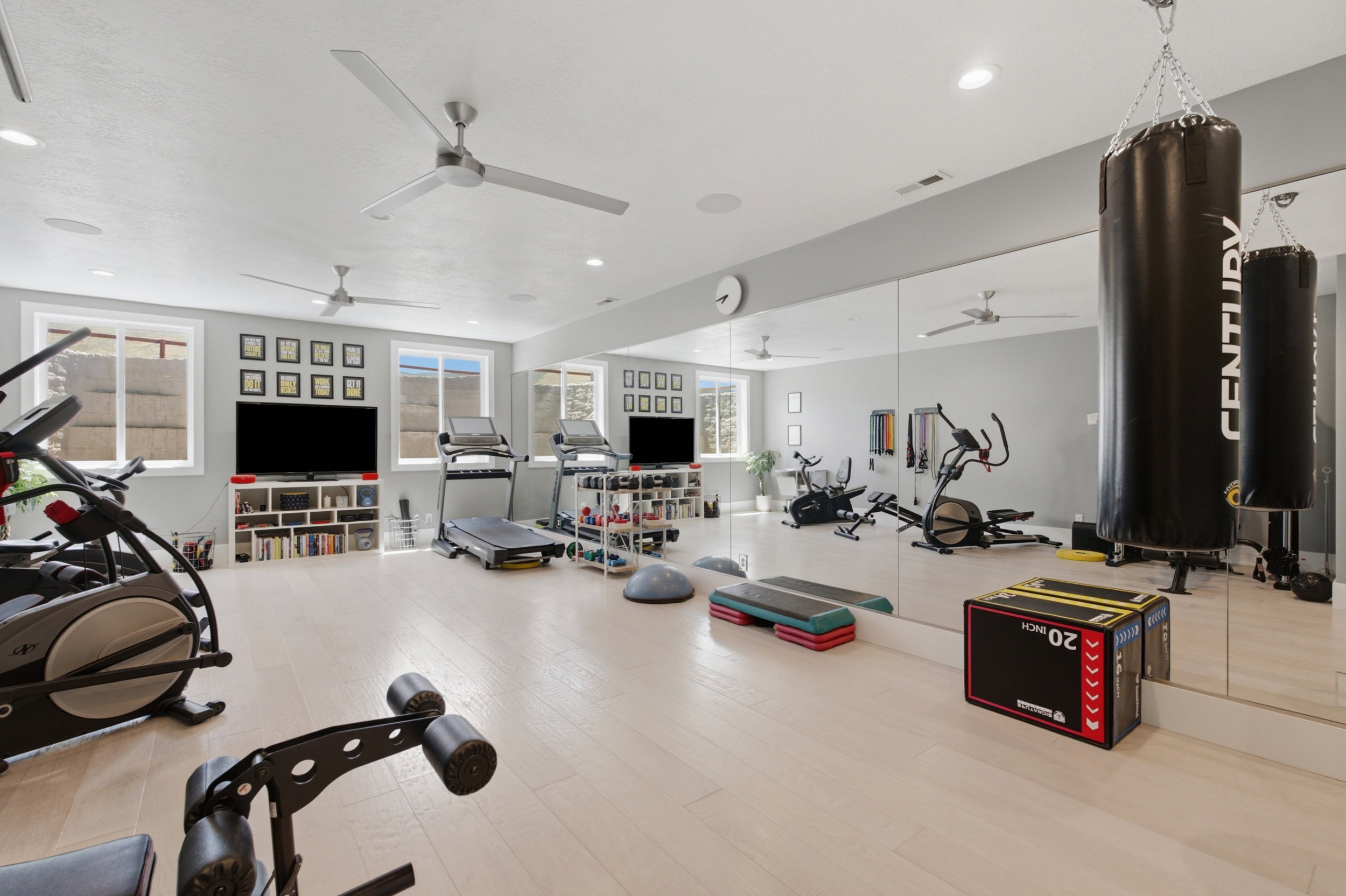 Dedicated fitness space featuring light wood-finish flooring, full-wall mirrors, recessed lighting, and multiple ceiling fans
