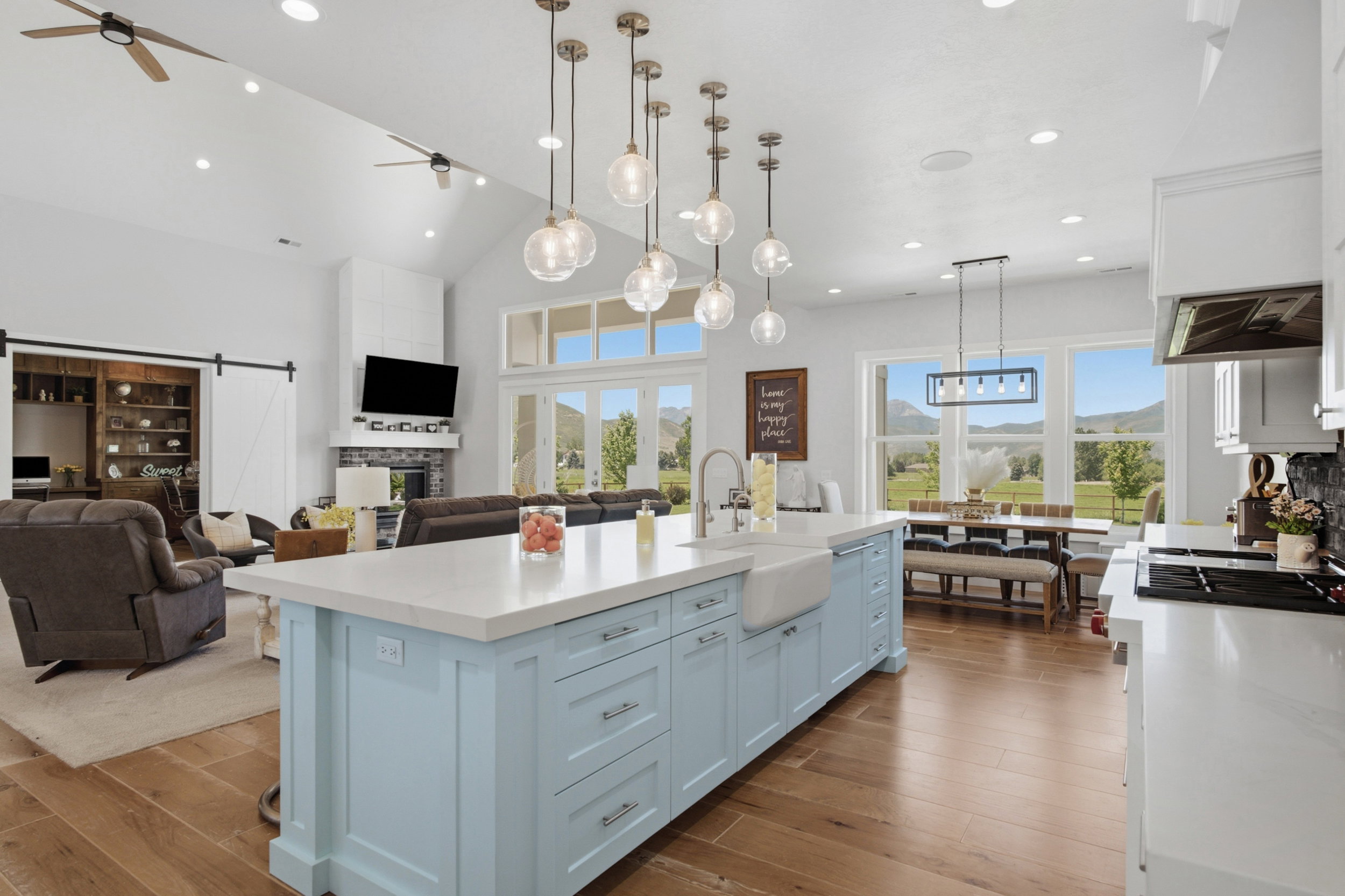 Spacious kitchen featuring a light blue island with a farmhouse sink and pendant lighting, white cabinetry, and wood-finish flooring
