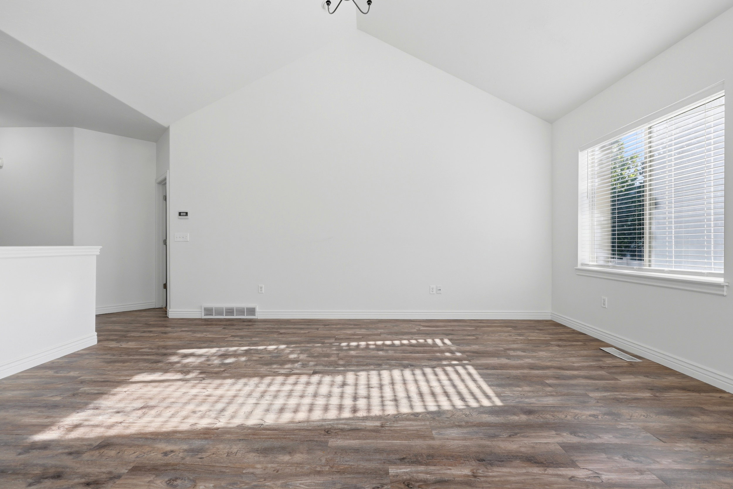 Spacious room featuring vaulted ceilings, wood-finish flooring, white baseboards, and a large window with white blinds