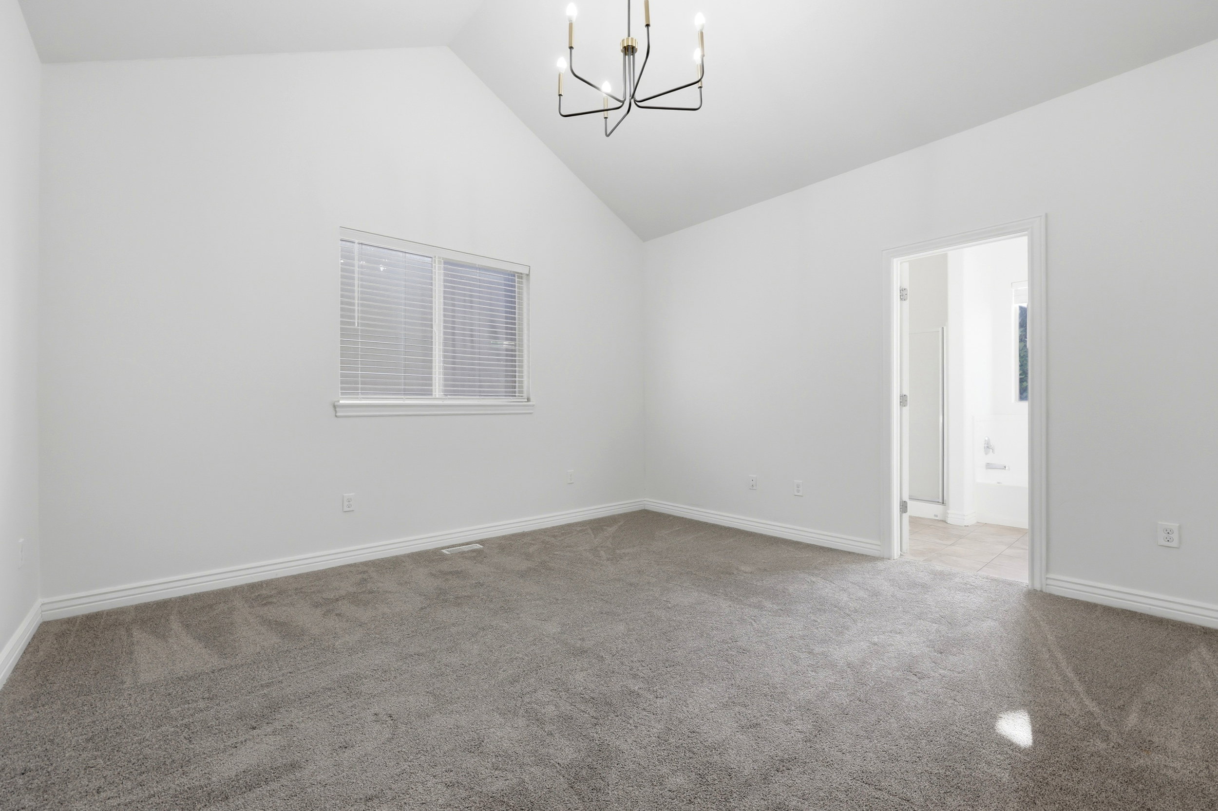Spacious room featuring vaulted ceilings, a contemporary ceiling light fixture, grey carpet flooring, and a window with horizontal blinds