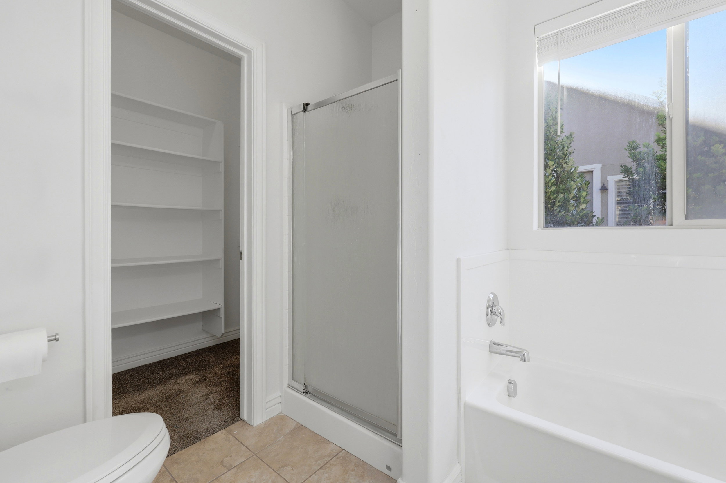 Bathroom featuring a built-in bathtub with chrome fixtures, a separate shower enclosure with a frosted glass door, and tiled flooring