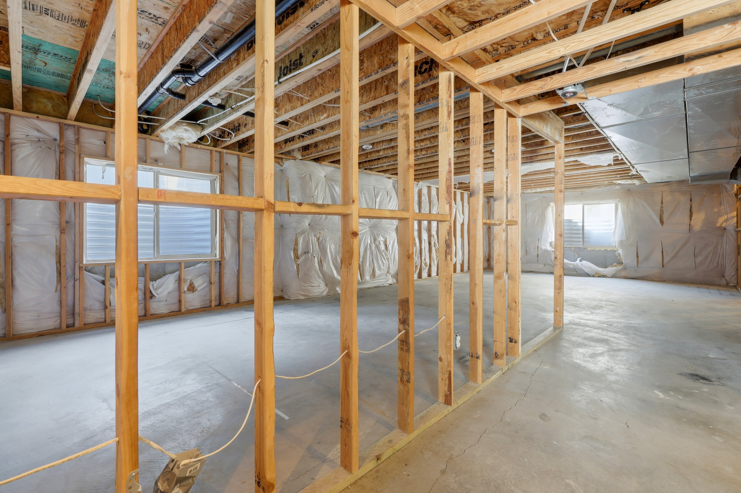 Unfinished basement featuring extensive framing, concrete flooring, exposed joists, visible ductwork, and multiple egress windows