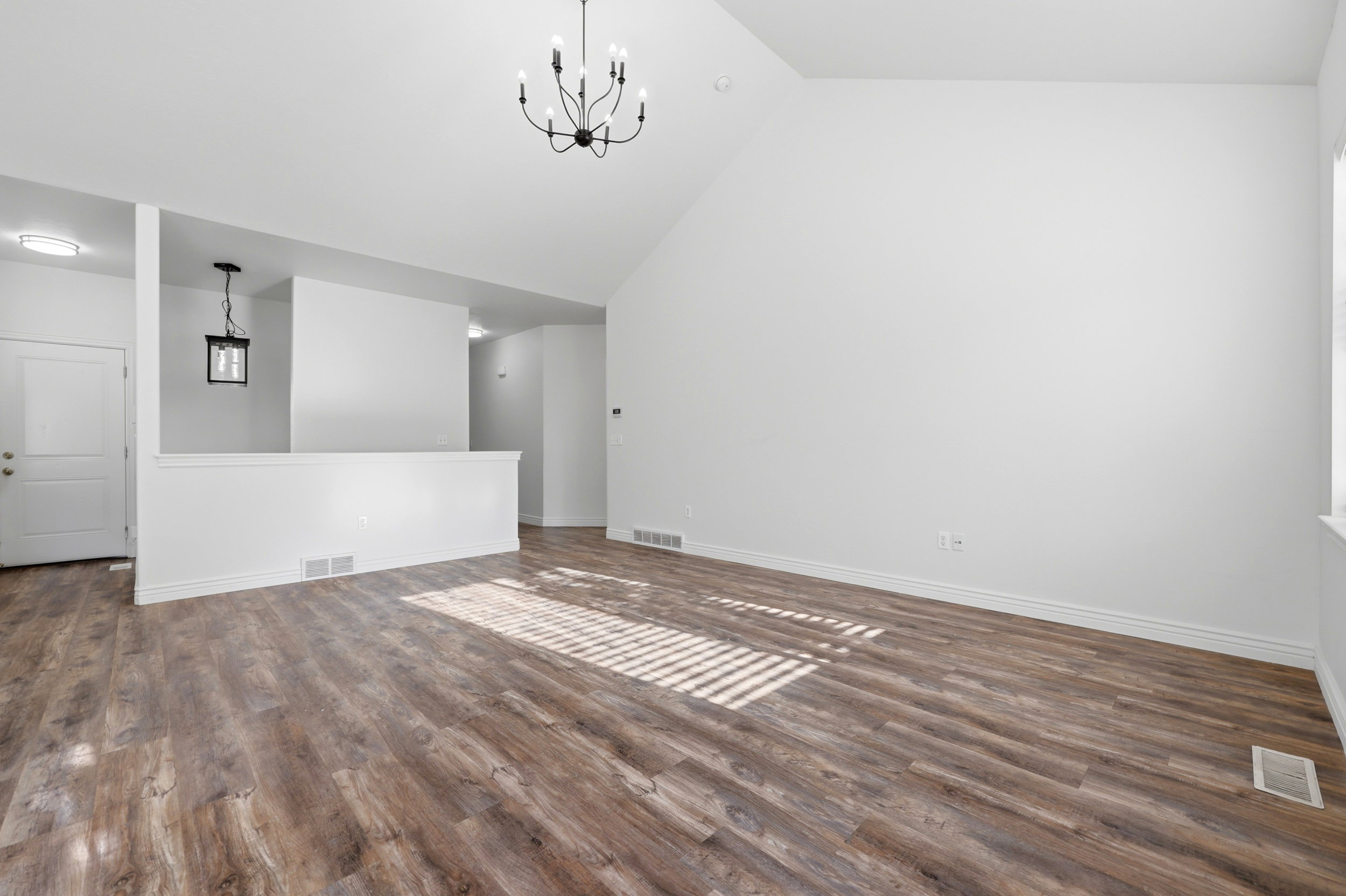 Spacious interior featuring wood-finish flooring, vaulted ceiling, and a modern black chandelier