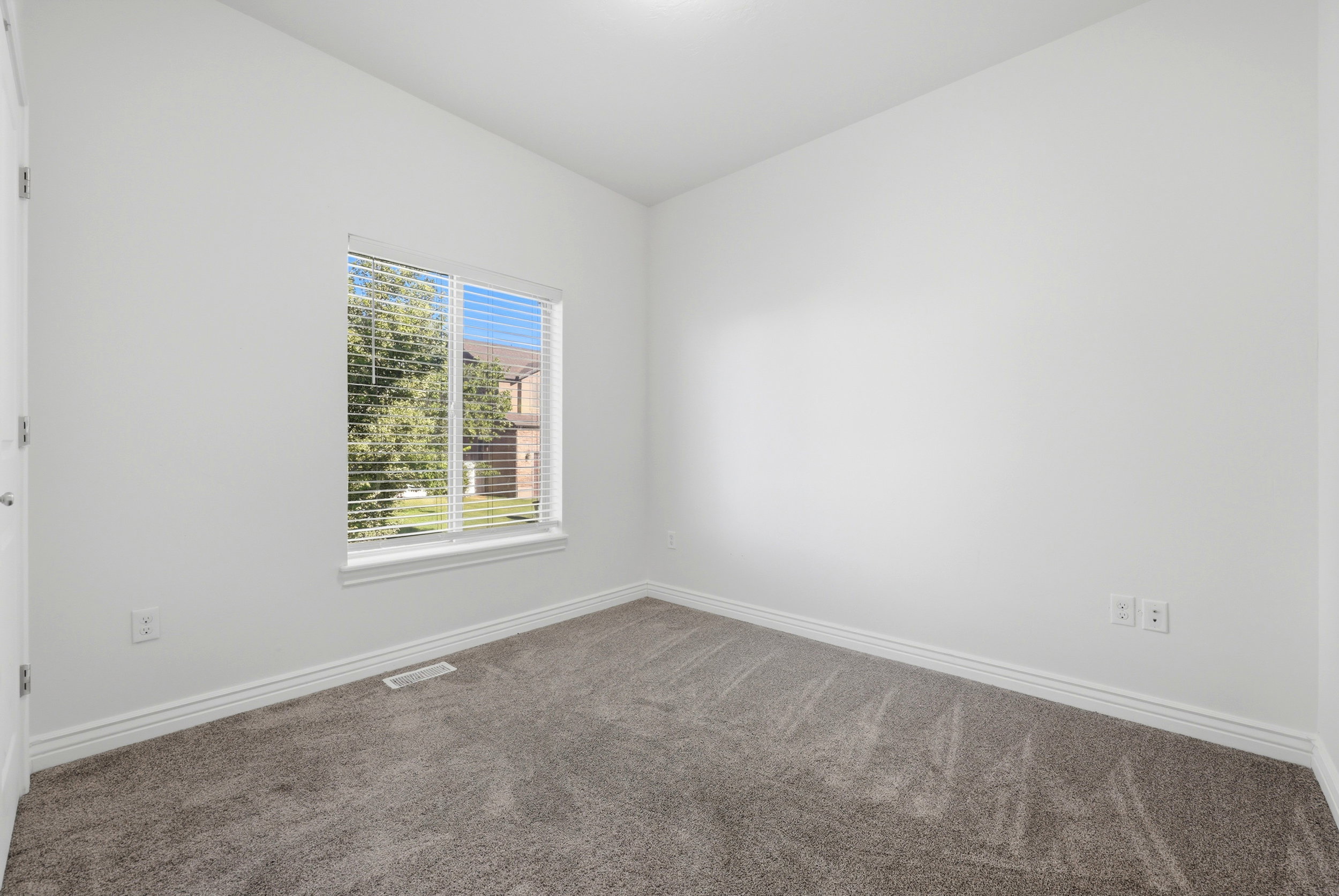 Neutral-toned room featuring a single window with blinds, light gray carpeting, white walls, and white baseboards