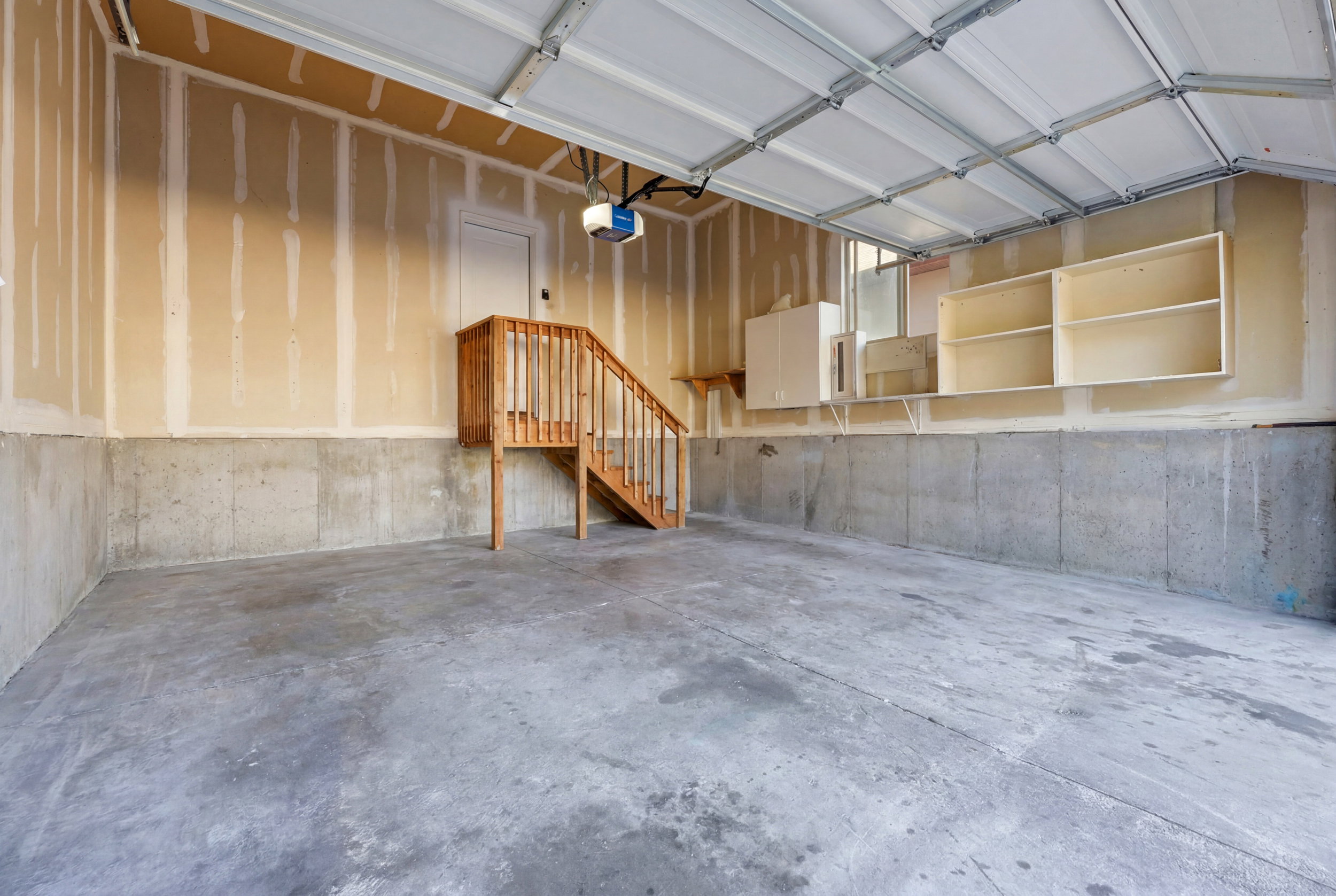 Spacious garage featuring a concrete floor, exposed drywall walls, a wooden staircase, and built-in storage shelving