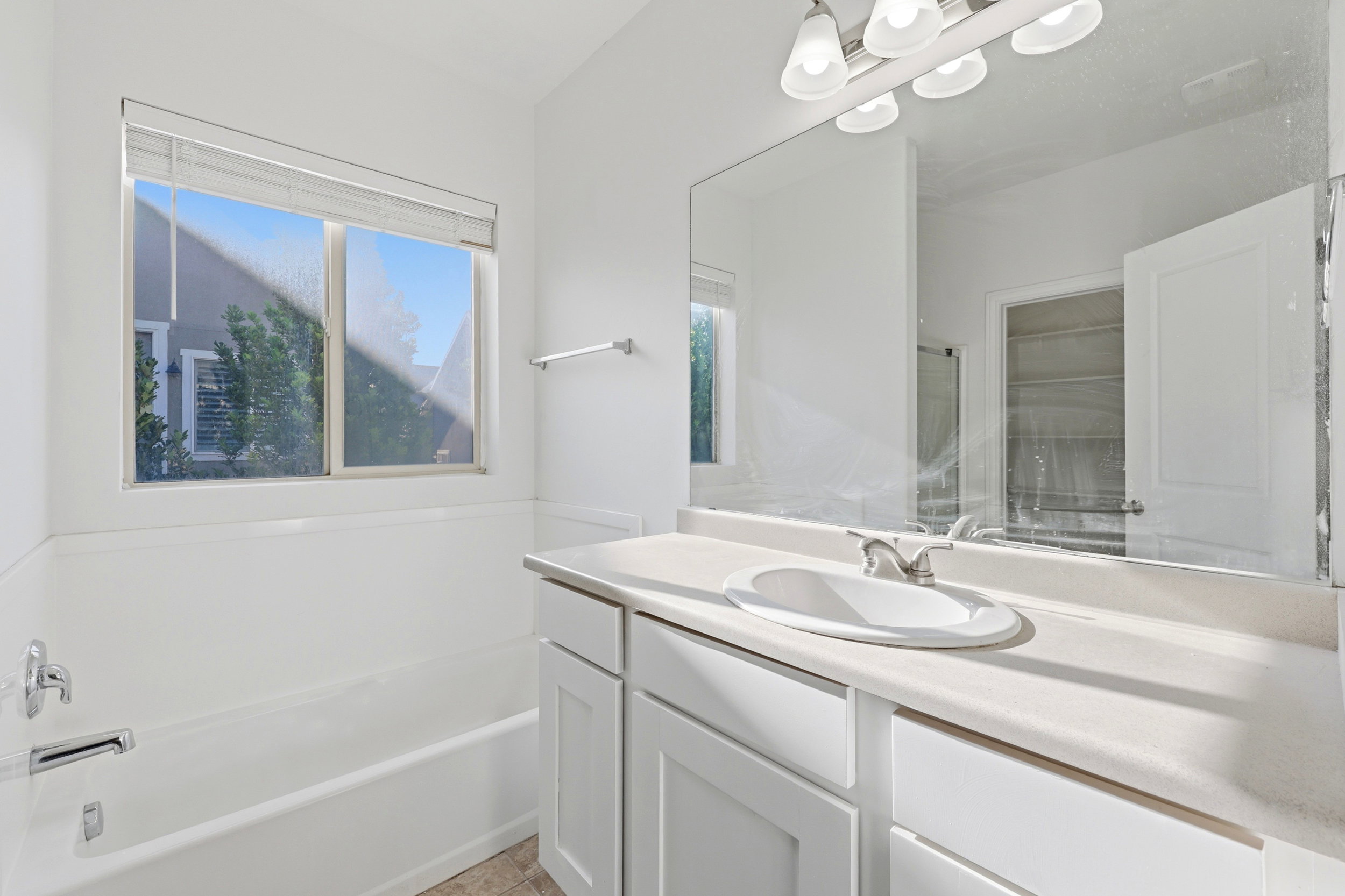 White vanity with a single basin sink, a large wall-mounted mirror, and a three-light fixture