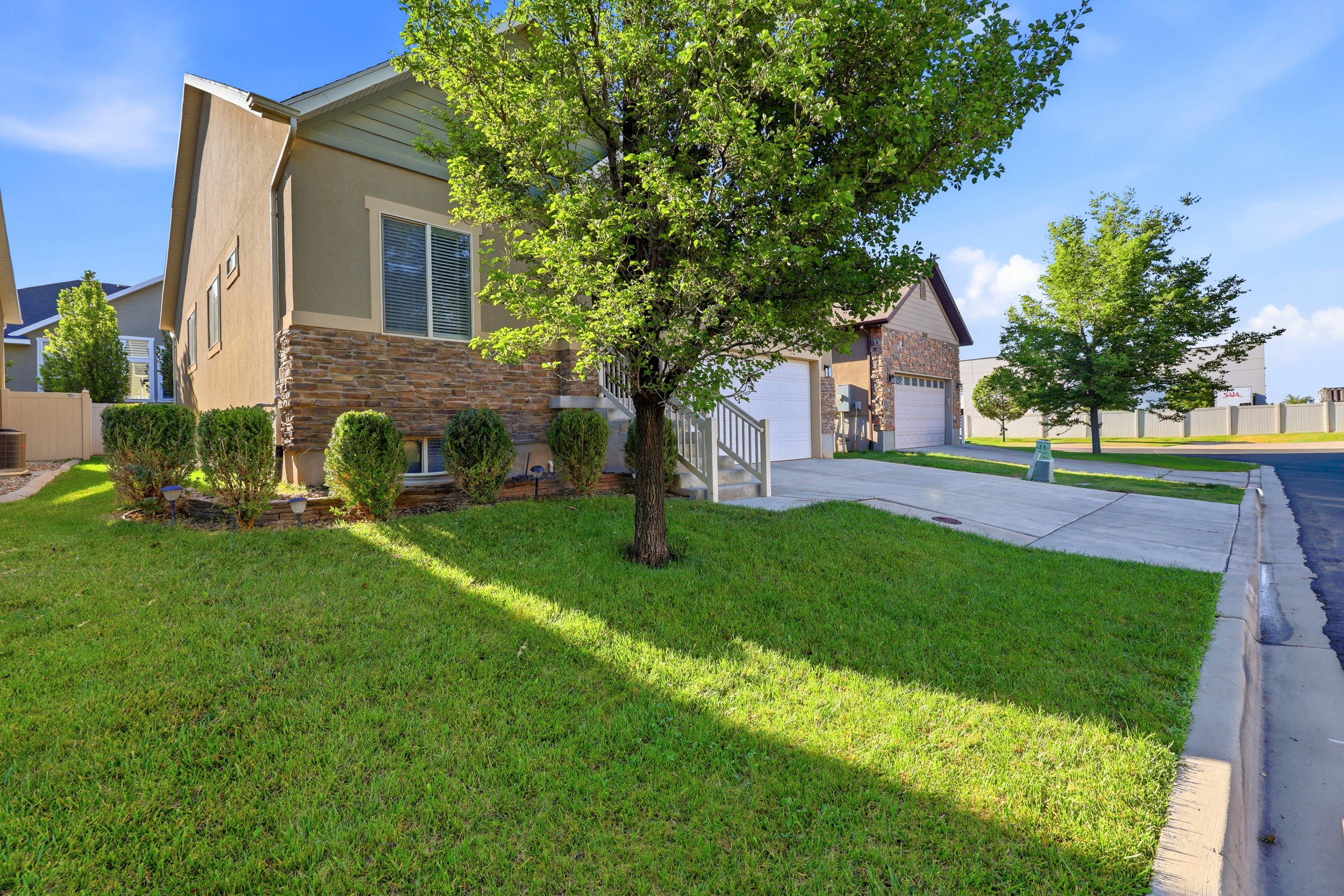 Exterior facade featuring a stucco finish with a stacked stone accent, a manicured lawn, established shrubs, and a mature tree