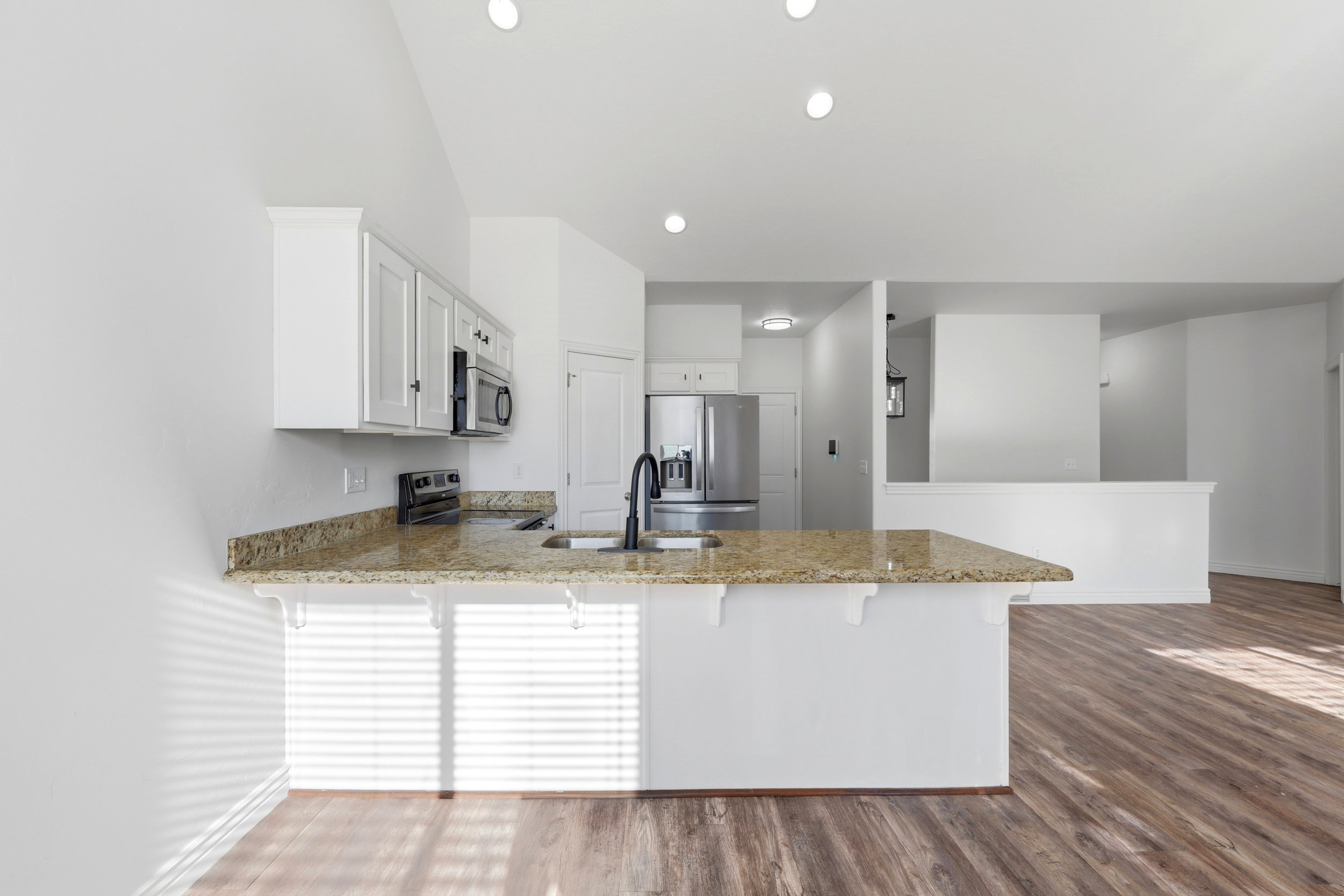 Modern kitchen featuring white cabinetry, granite countertops, wood-finish flooring, stainless steel appliances, and recessed lighting
