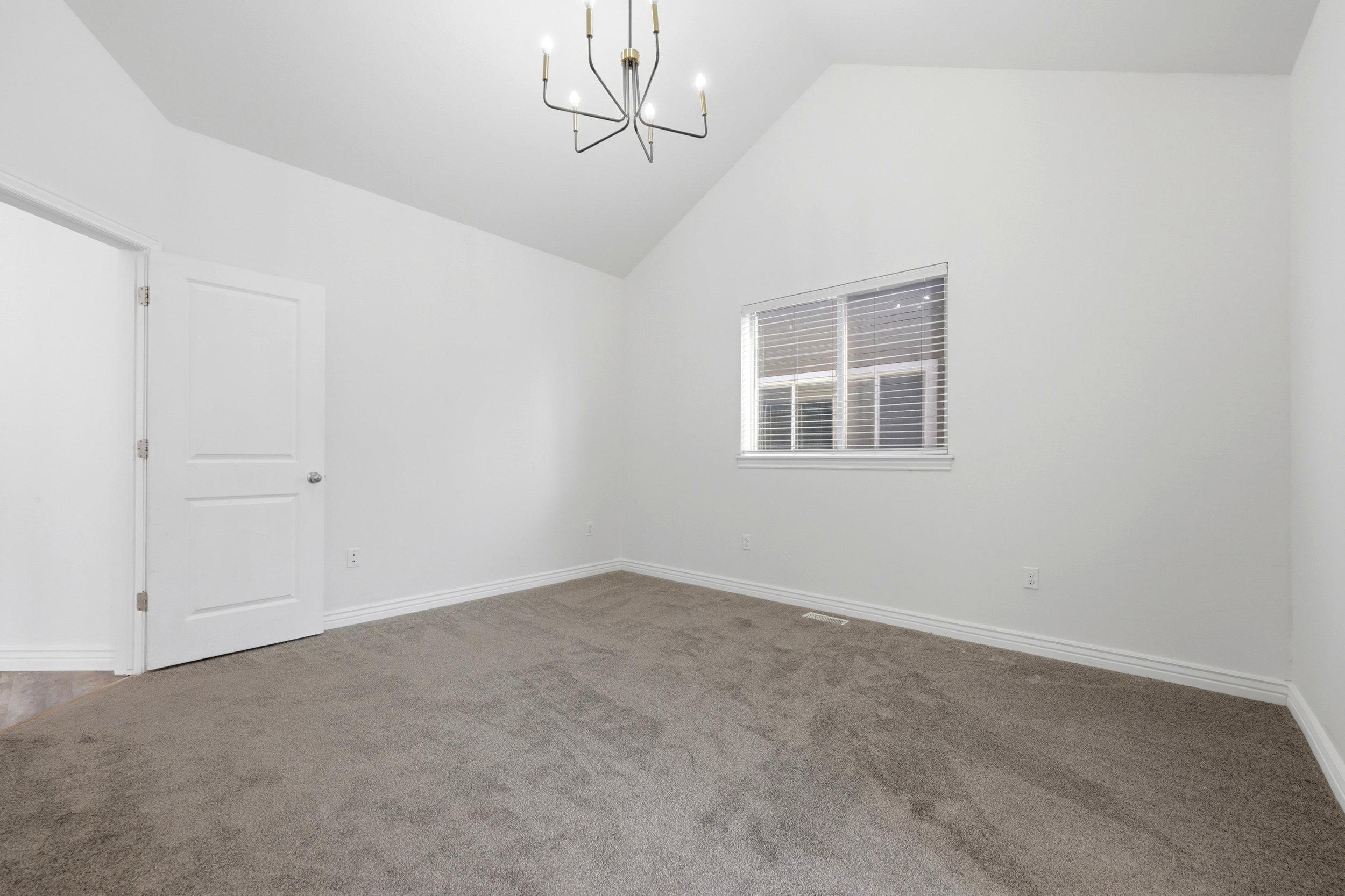 Vaulted ceiling room with neutral carpet flooring, white painted walls, and a contemporary chandelier
