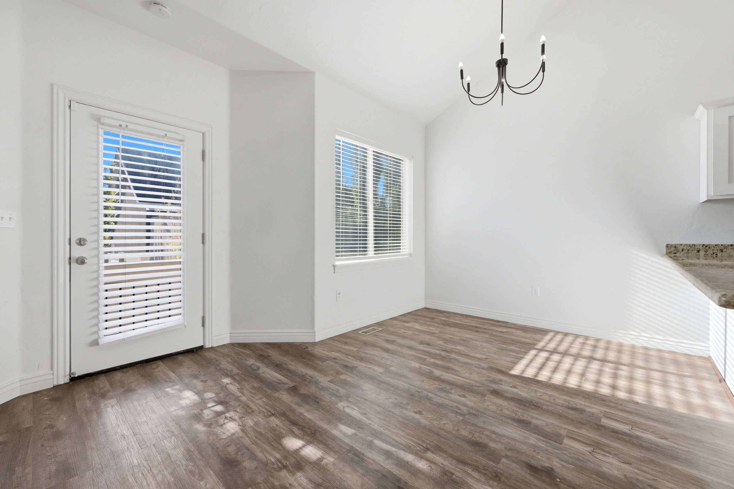 Open-concept area featuring wood-finish flooring, white walls, and a contemporary black chandelier