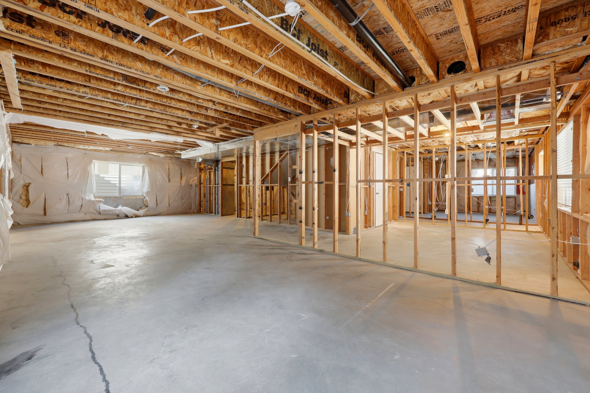 Unfinished basement featuring exposed wood joists, framed interior walls, concrete flooring, and a visible window with horizontal blinds